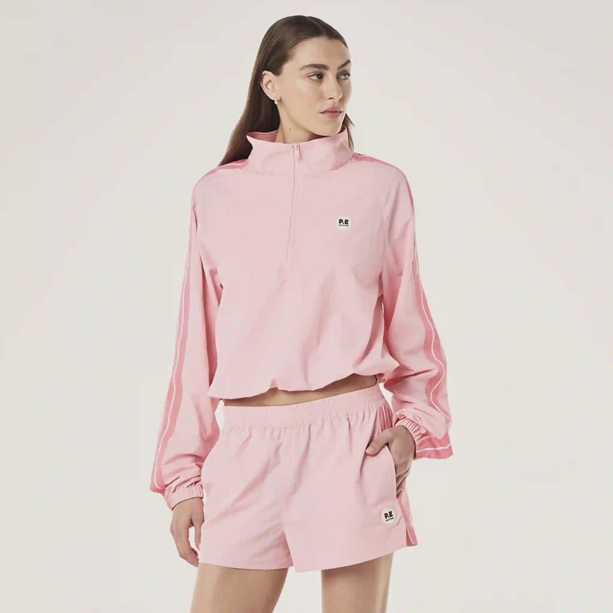 Person wearing a pink tracksuit with a small logo on a plain background