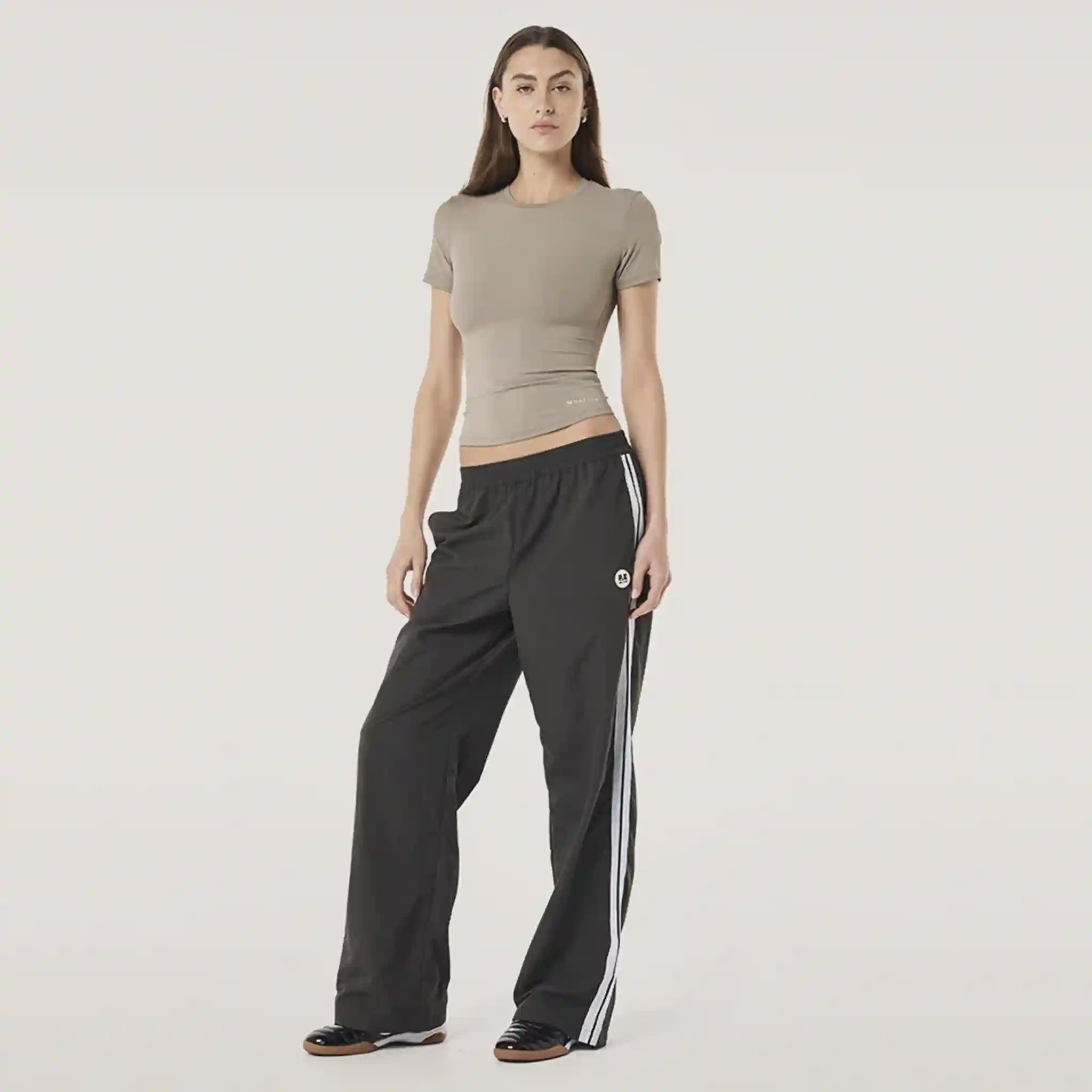 Woman wearing a gray crop top and black pants with white stripes on a light gray background