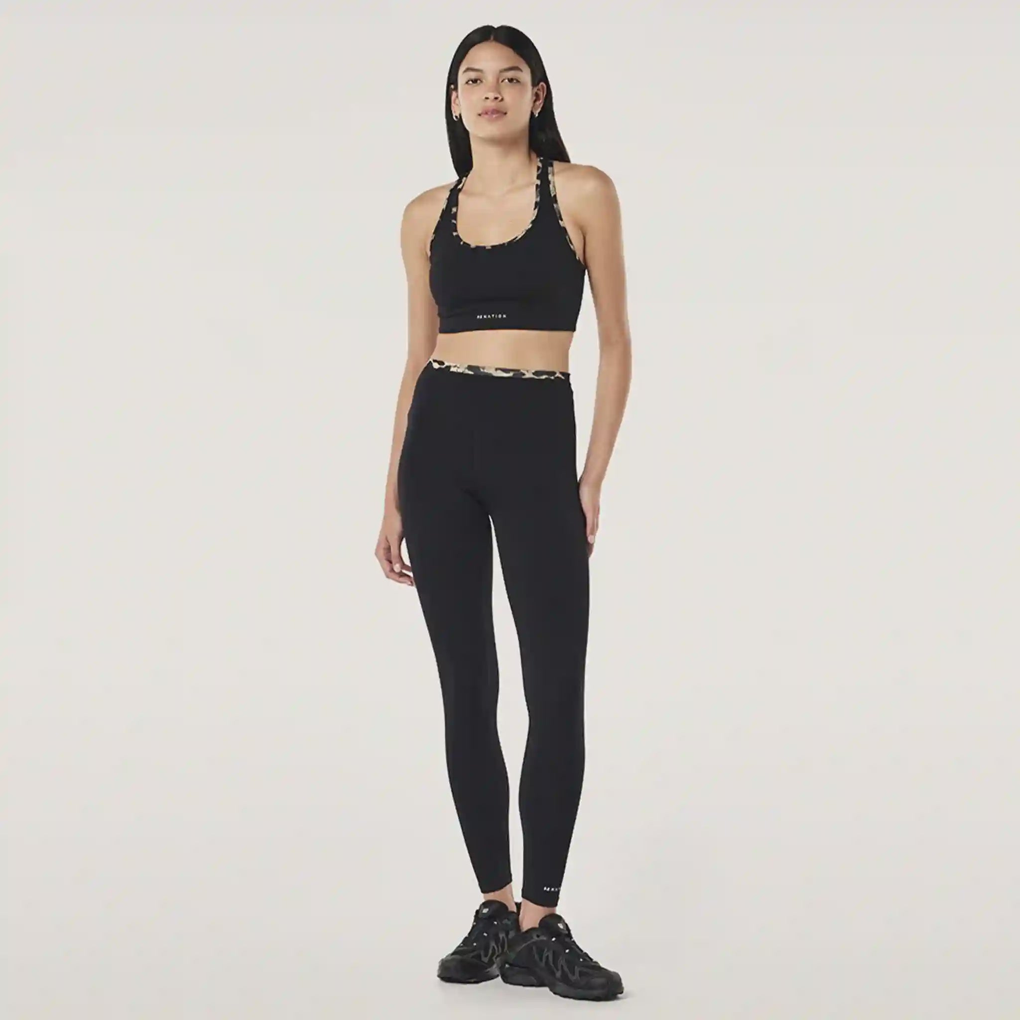 Woman wearing a black sports bra and leggings set on a white background