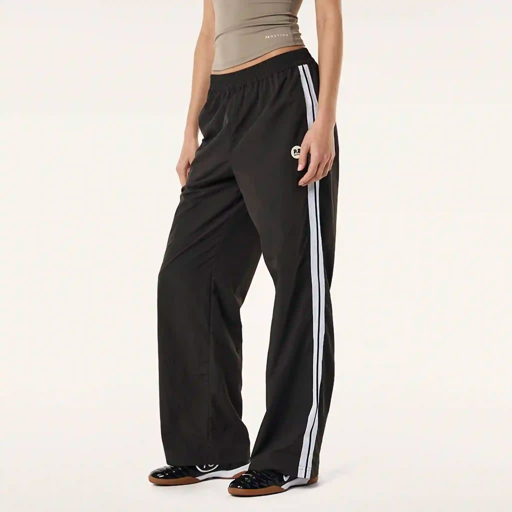Black track pants with white stripes worn by a person on a plain background