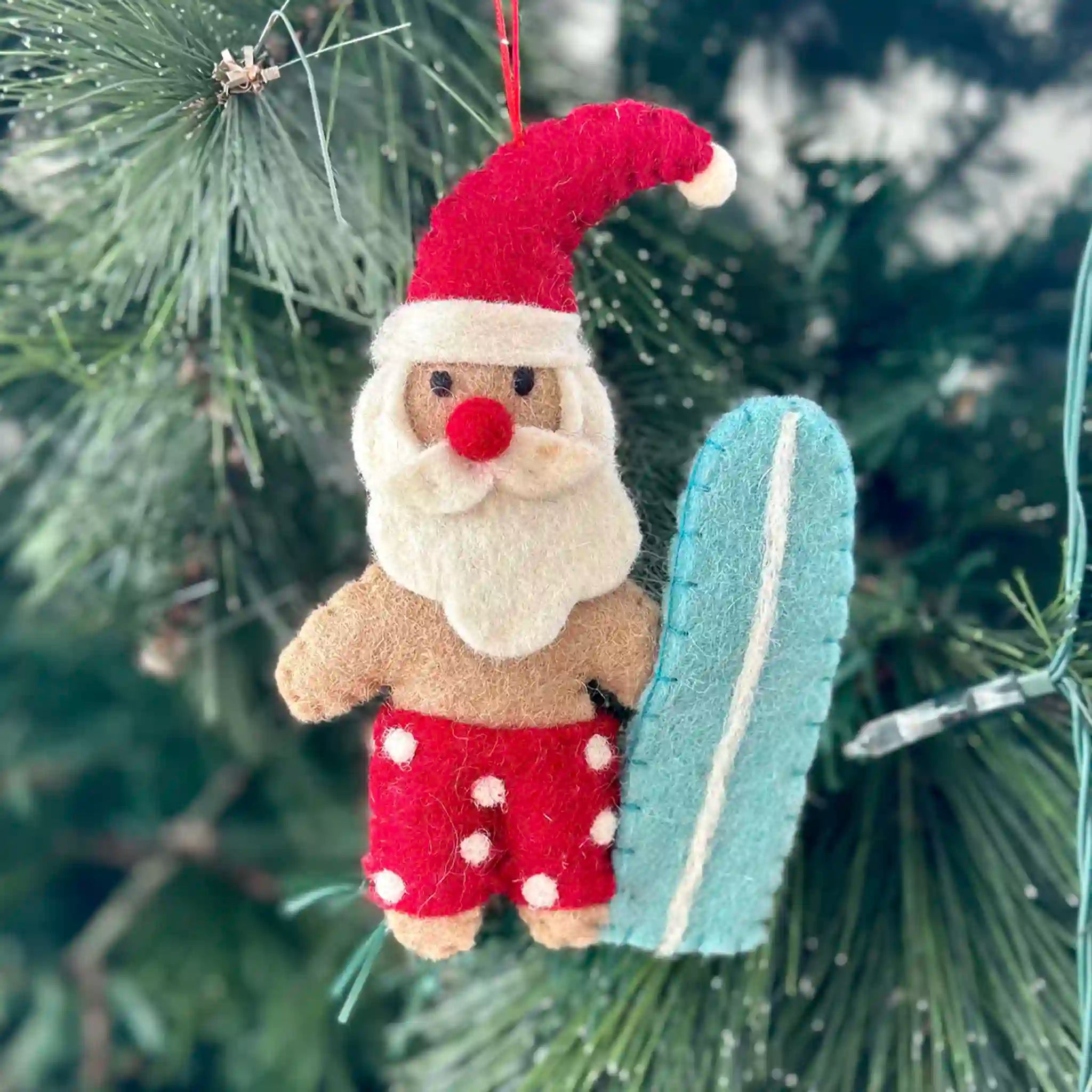 Felt Santa Claus ornament with a surfboard hanging on a Christmas tree.