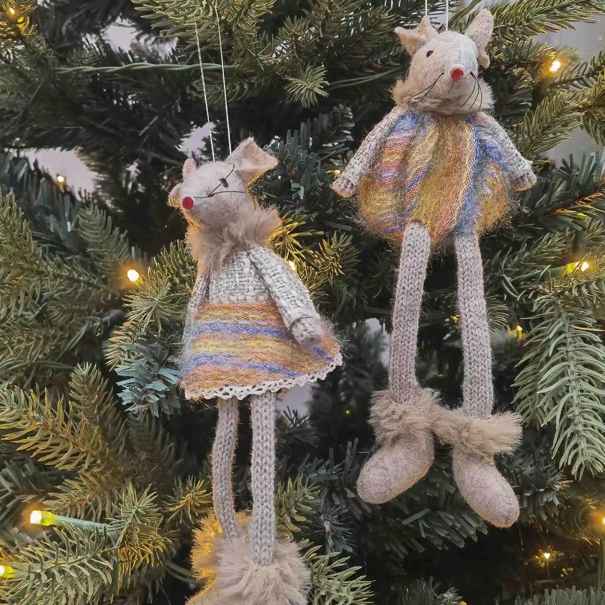 Two knitted mouse ornaments hanging on a decorated Christmas tree.