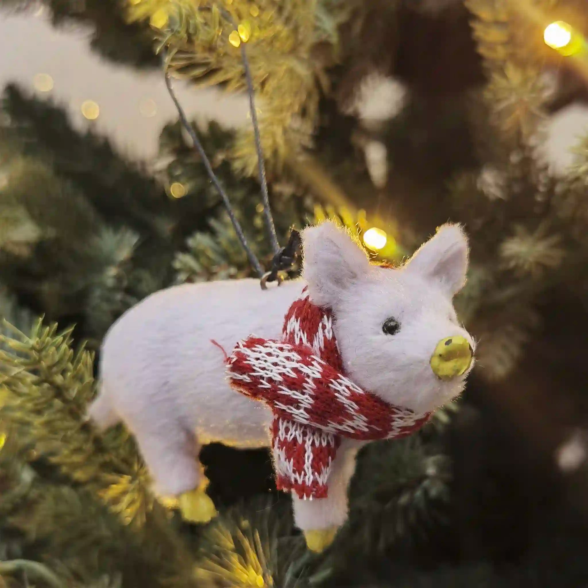 White pig ornament with a red and white scarf on a Christmas tree.