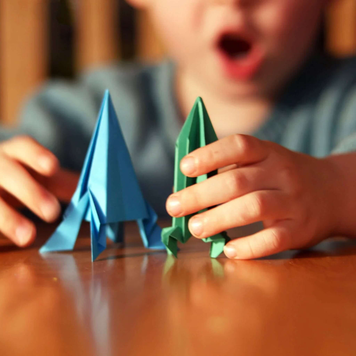 Child holding blue and green origami rockets from Pikkii Origami Paper Flying Rockets set.