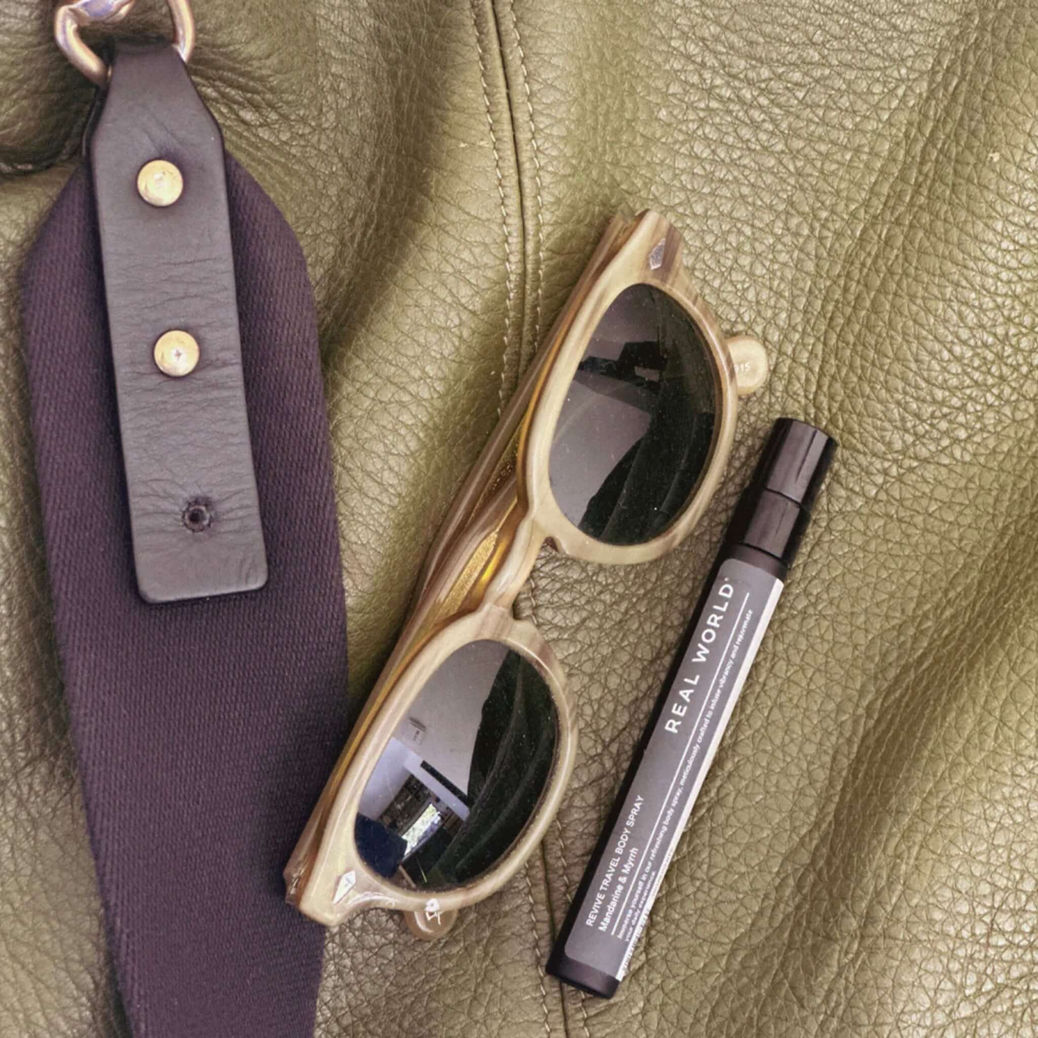 Alt Tag: Real World NZ Travel Body Spray 10ml body spray bottle beside sunglasses on leather bag, refreshing on-the-go travel scent