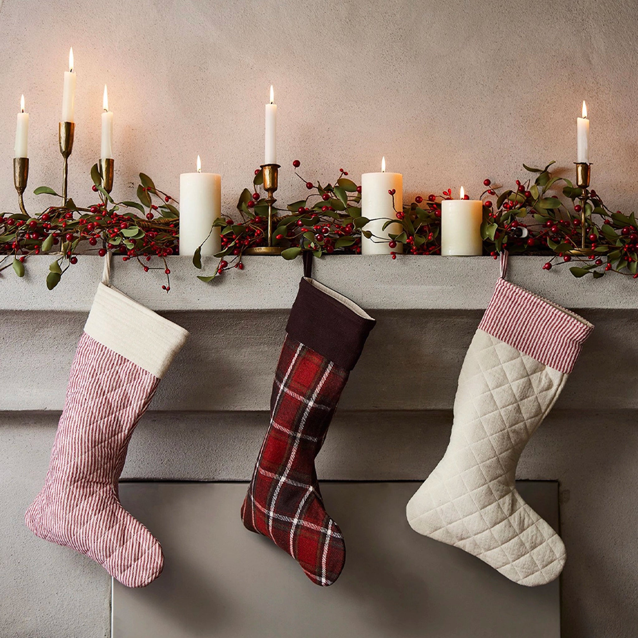 Three Christmas stockings hanging by a fireplace with candles and greenery.