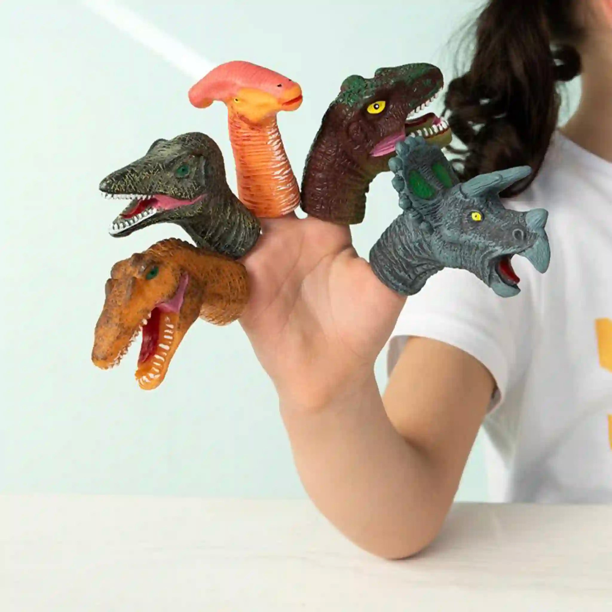 Person wearing dinosaur finger puppets on their fingers against a white background