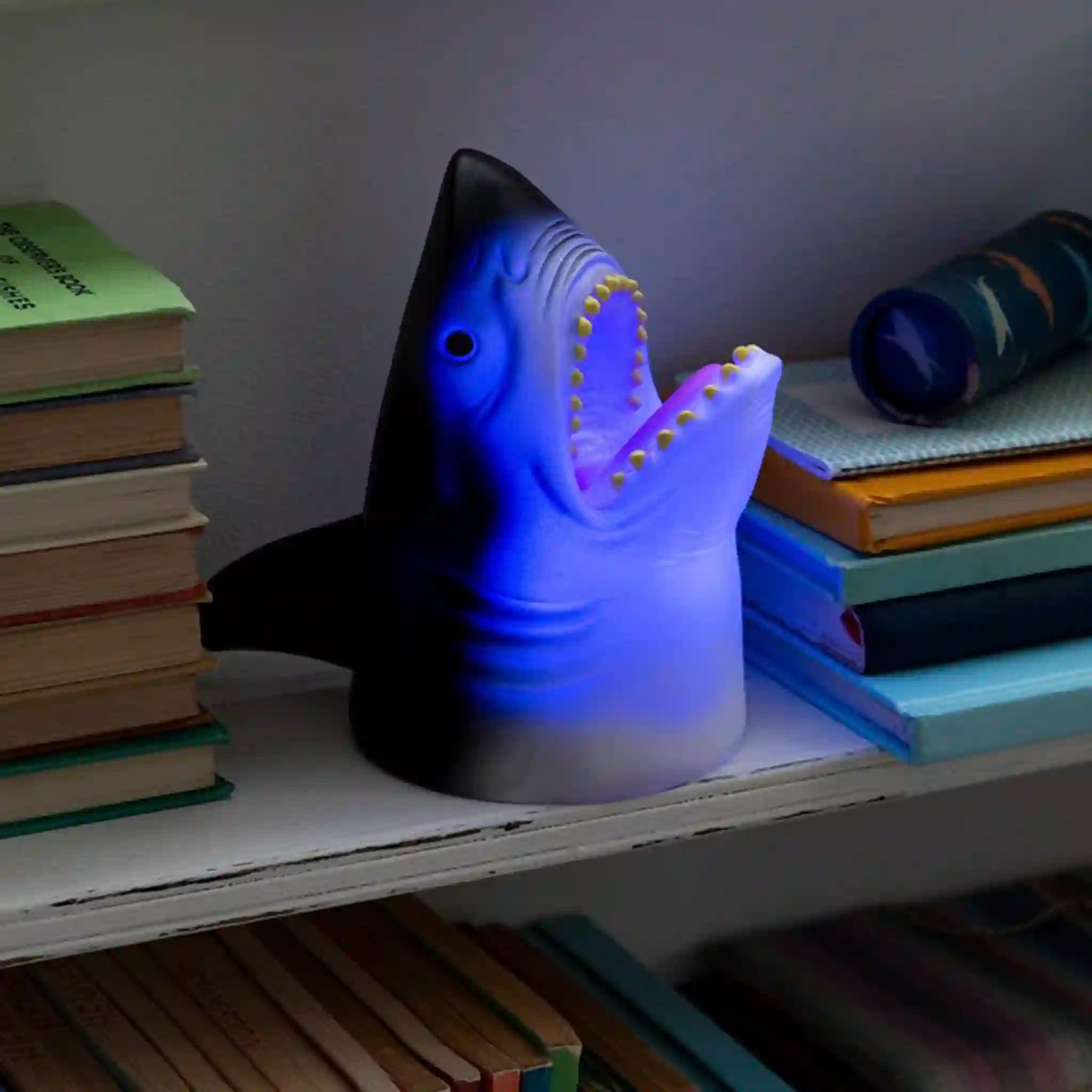 Shark-shaped night light on a bookshelf with books around