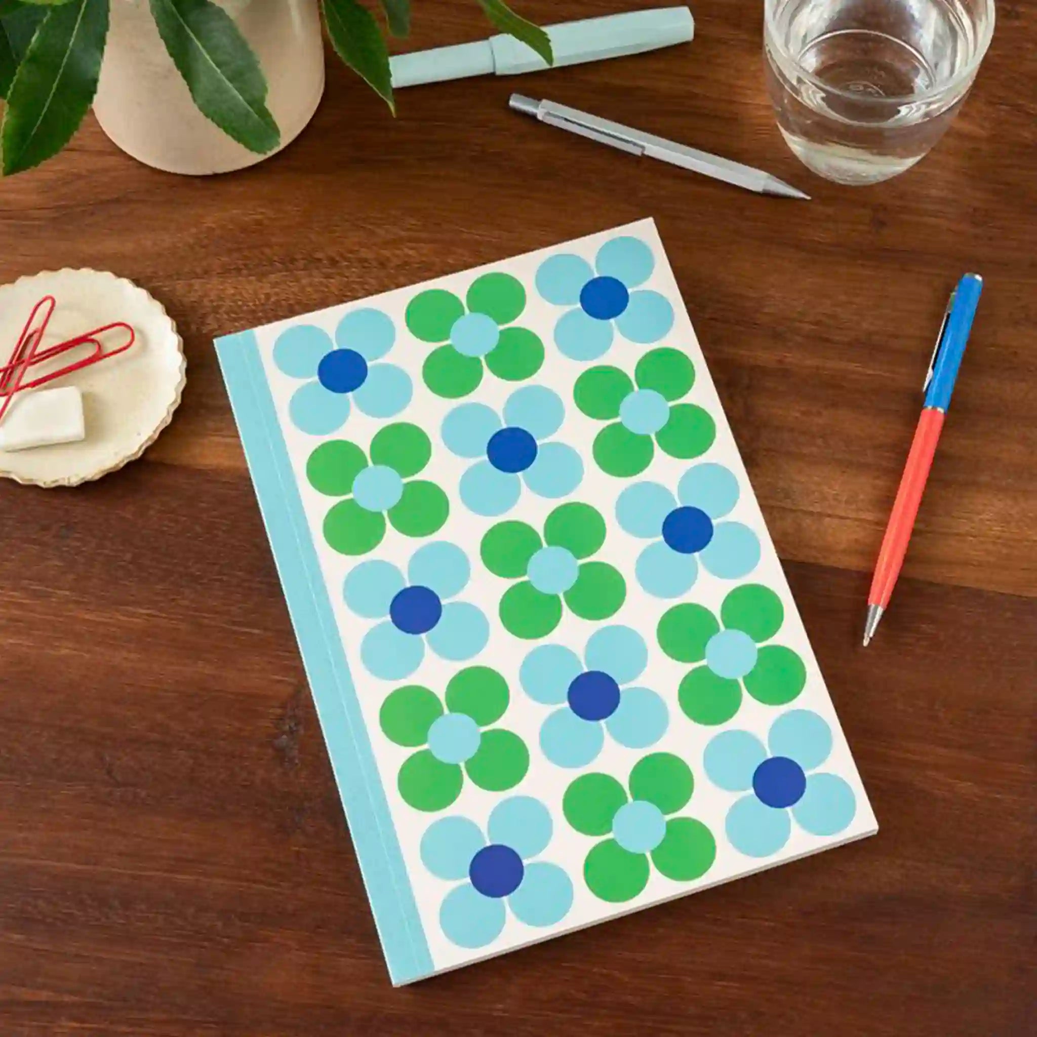 Notebook with blue and green floral pattern on a wooden surface with stationery items.