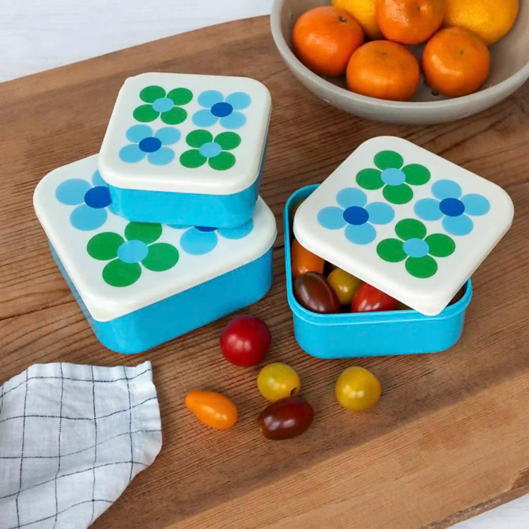 Two blue and white snack containers with floral lids on a wooden surface with fruits.