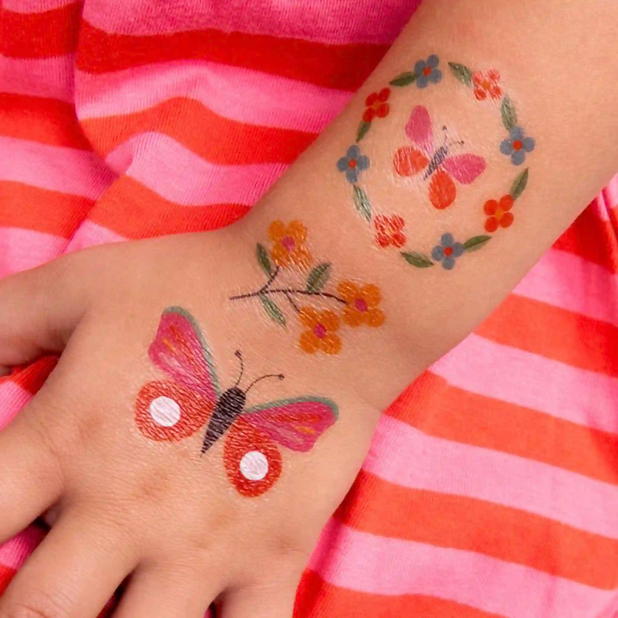Butterfly and floral temporary tattoos on a child's arm with a striped pink and orange background.