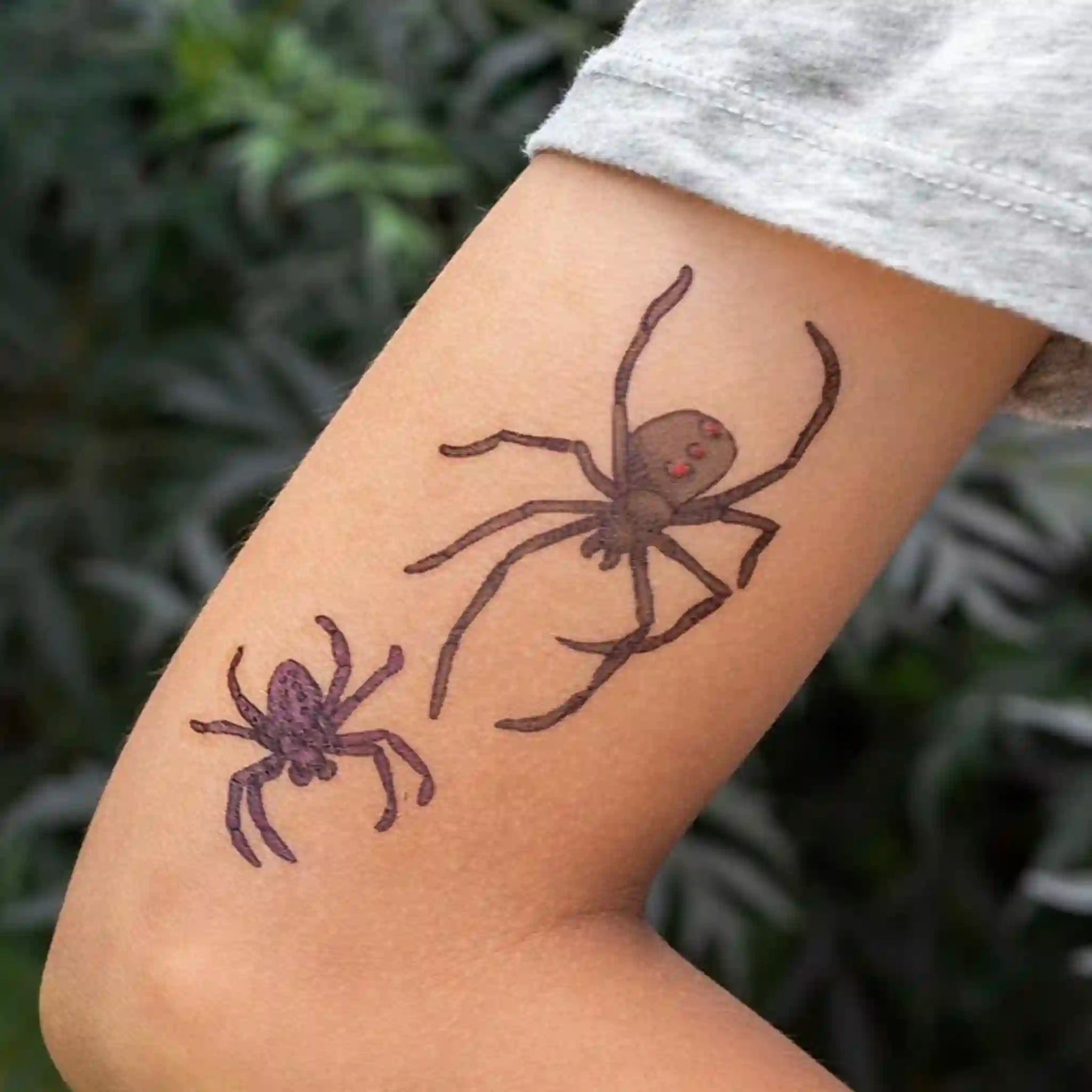Two spider tattoos on a person's arm with a blurred green background