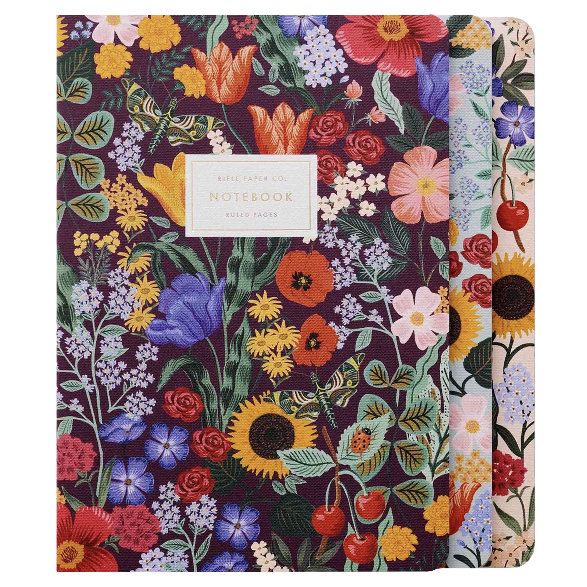 A set of three notebooks with a floral pattern on the covers, gold foil accents, and a white label with black text on the front.