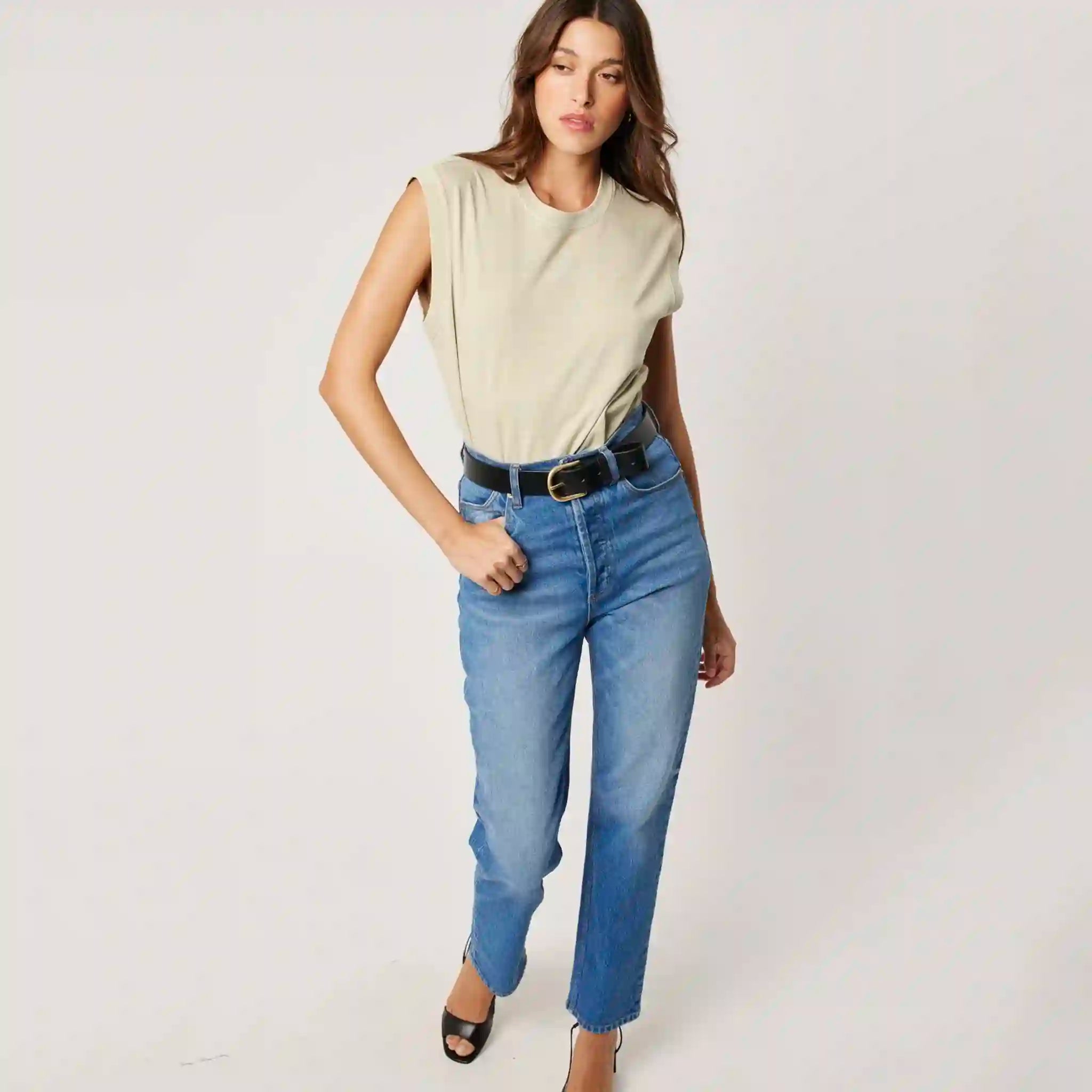 Woman wearing a beige sleeveless top and blue jeans on a white background