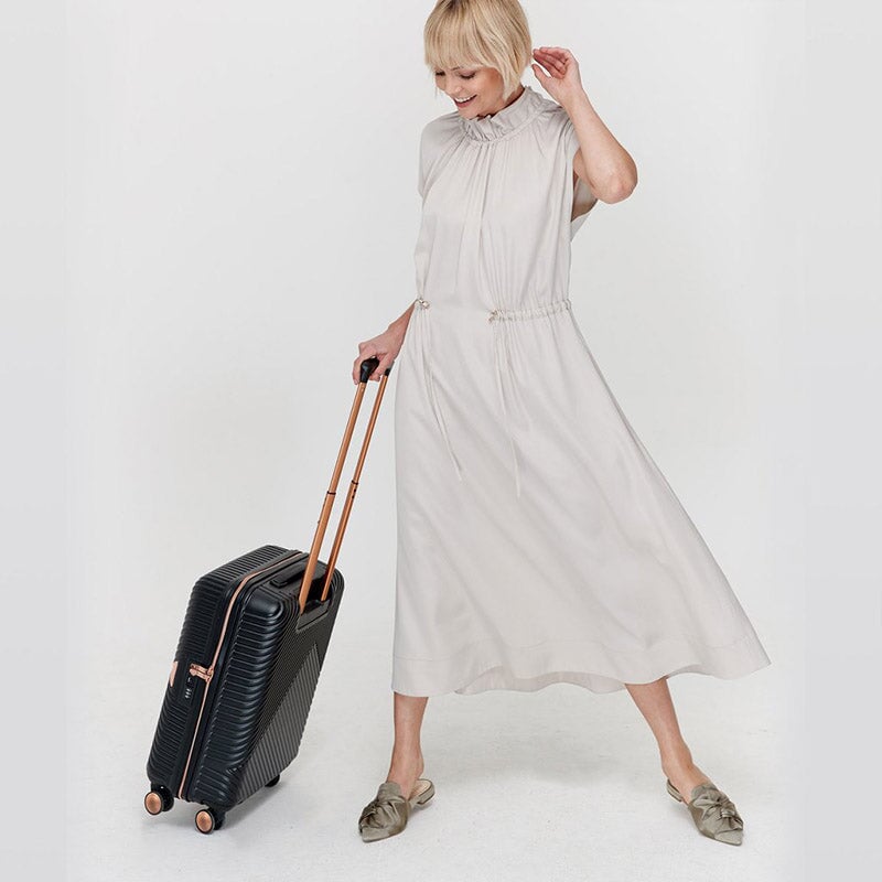 Woman holding a black cabin bag with metallic rose gold detailing, featuring a retractable handle and dual spinner wheels.