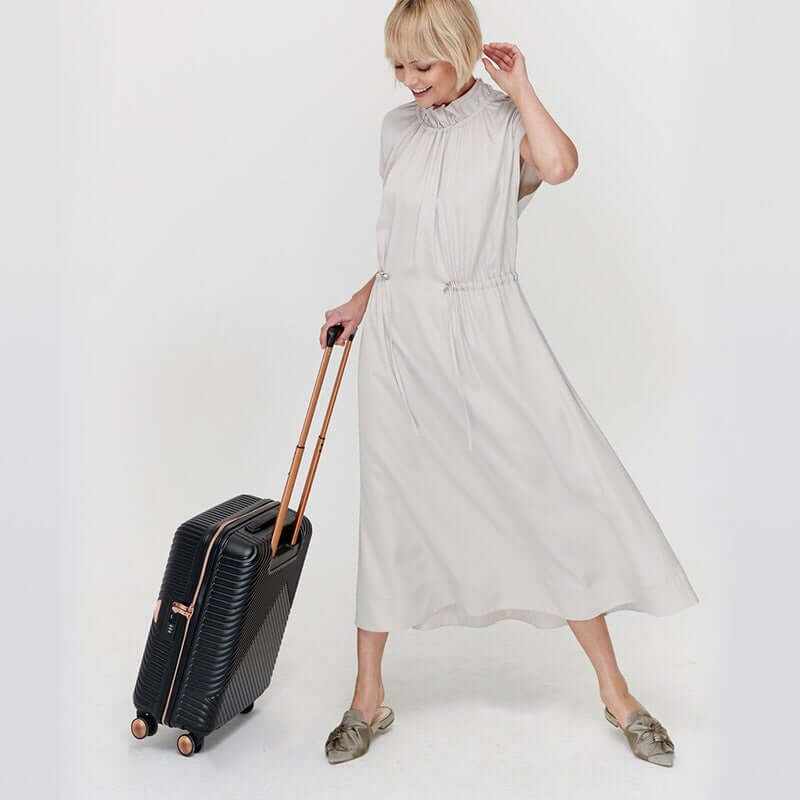 Woman holding a black cabin bag with metallic rose gold detailing, featuring a retractable handle and dual spinner wheels.