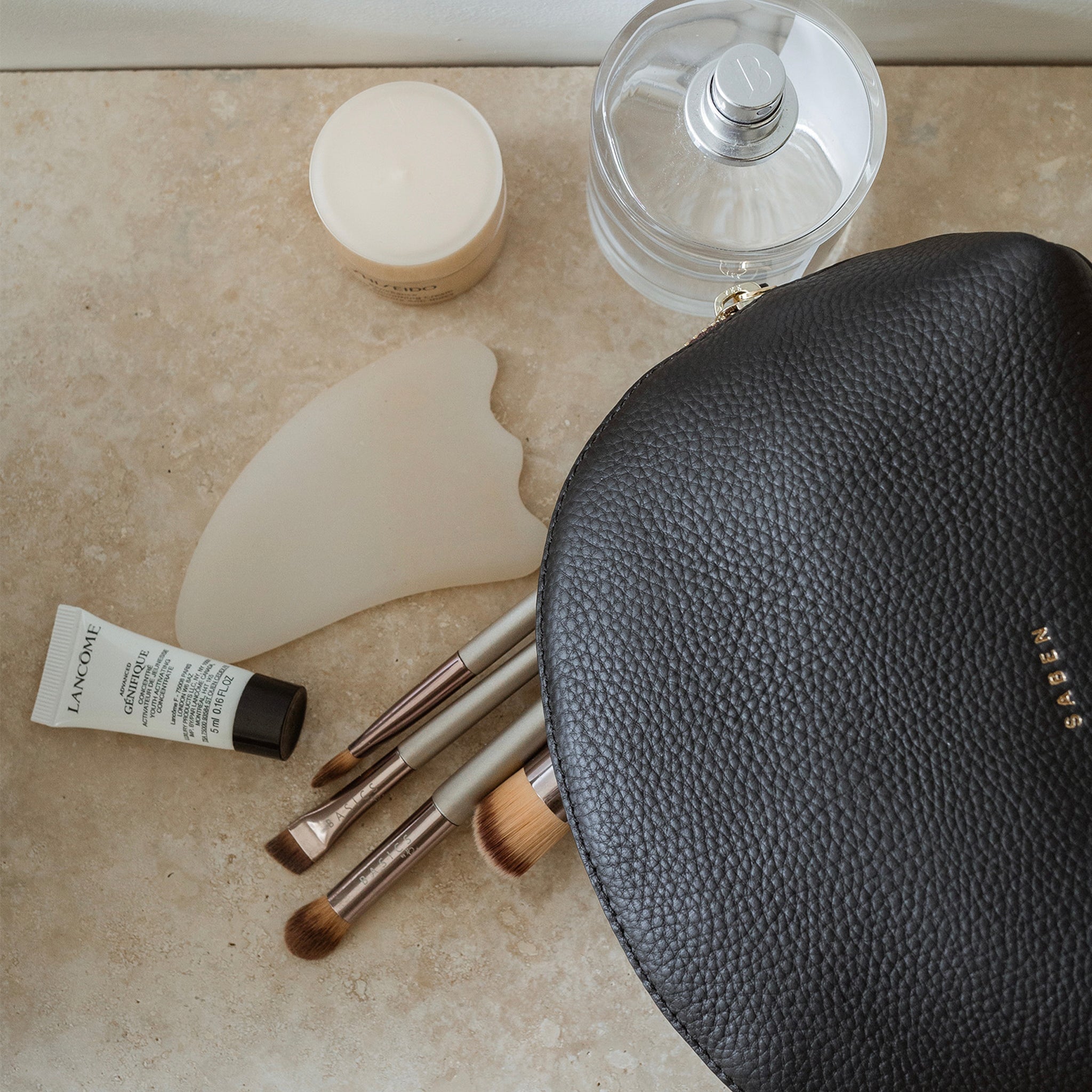 Black leather makeup bag with makeup brushes on a marble surface.