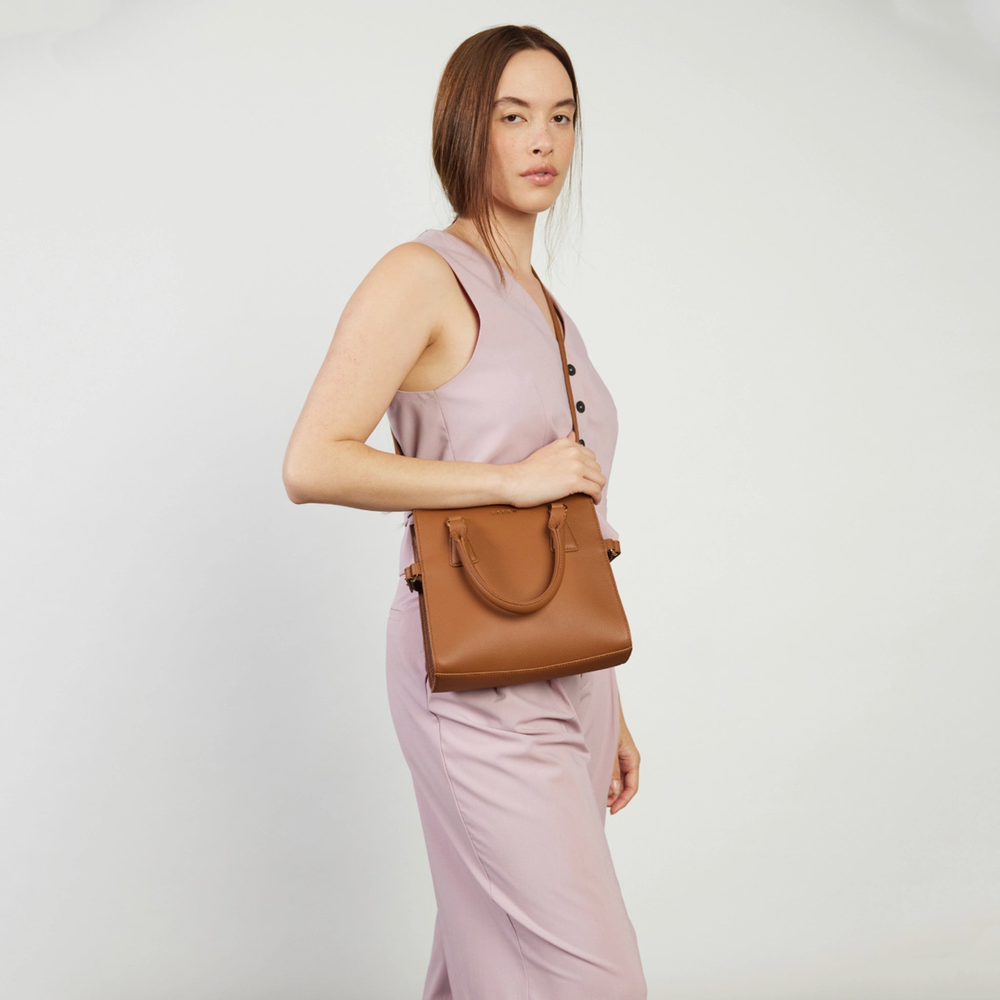 Woman holding a brown handbag against a plain background