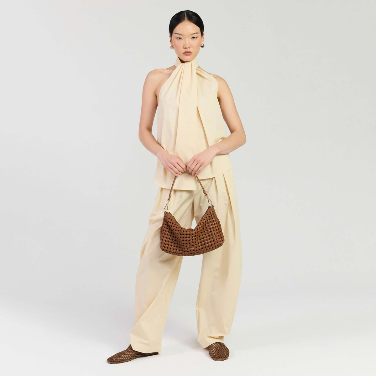 Saben Claudia Shoulder Bag - Tan Braid held by a model in a luxurious outfit, showcasing resort style fashion.