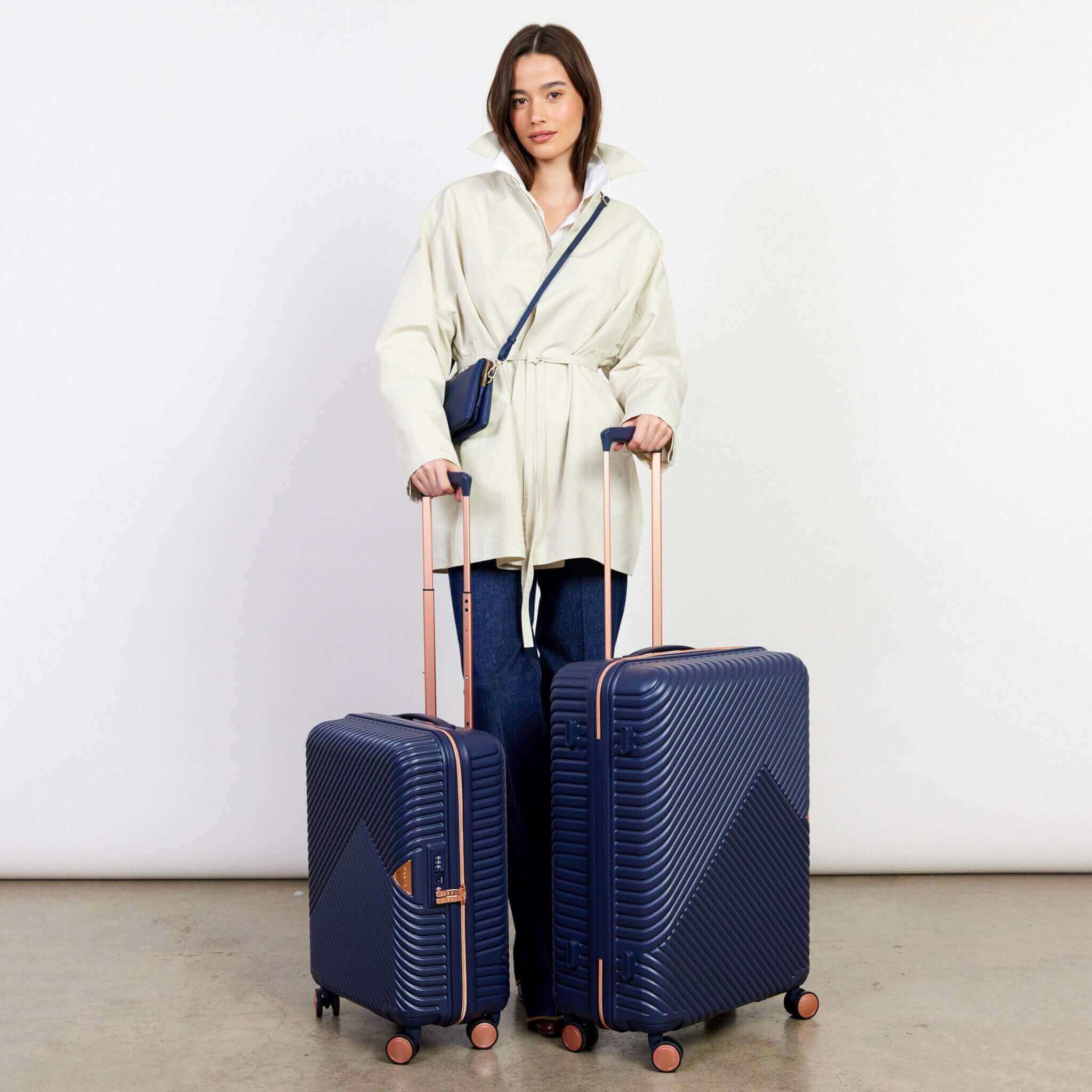 Woman holding two navy blue suitcases with a white background