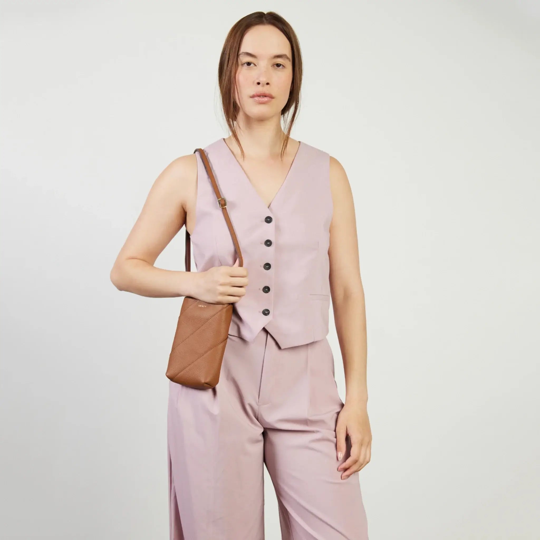 Person wearing a light pink vest and pants set with a brown bag on a white background