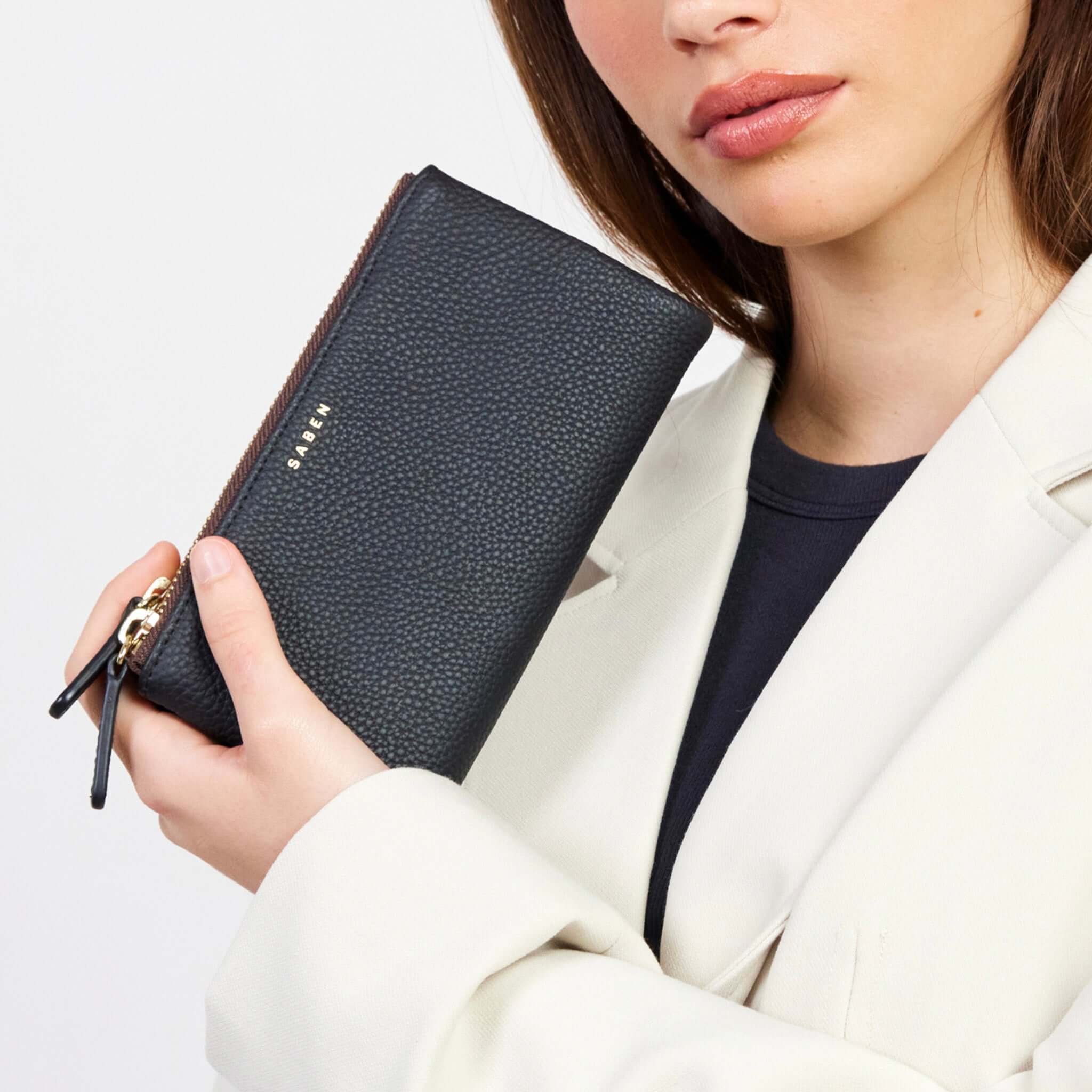 Alt Tag: Saben Sam Wallet - Black black leather wallet with gold hardware, held in hand, sleek slim zip design