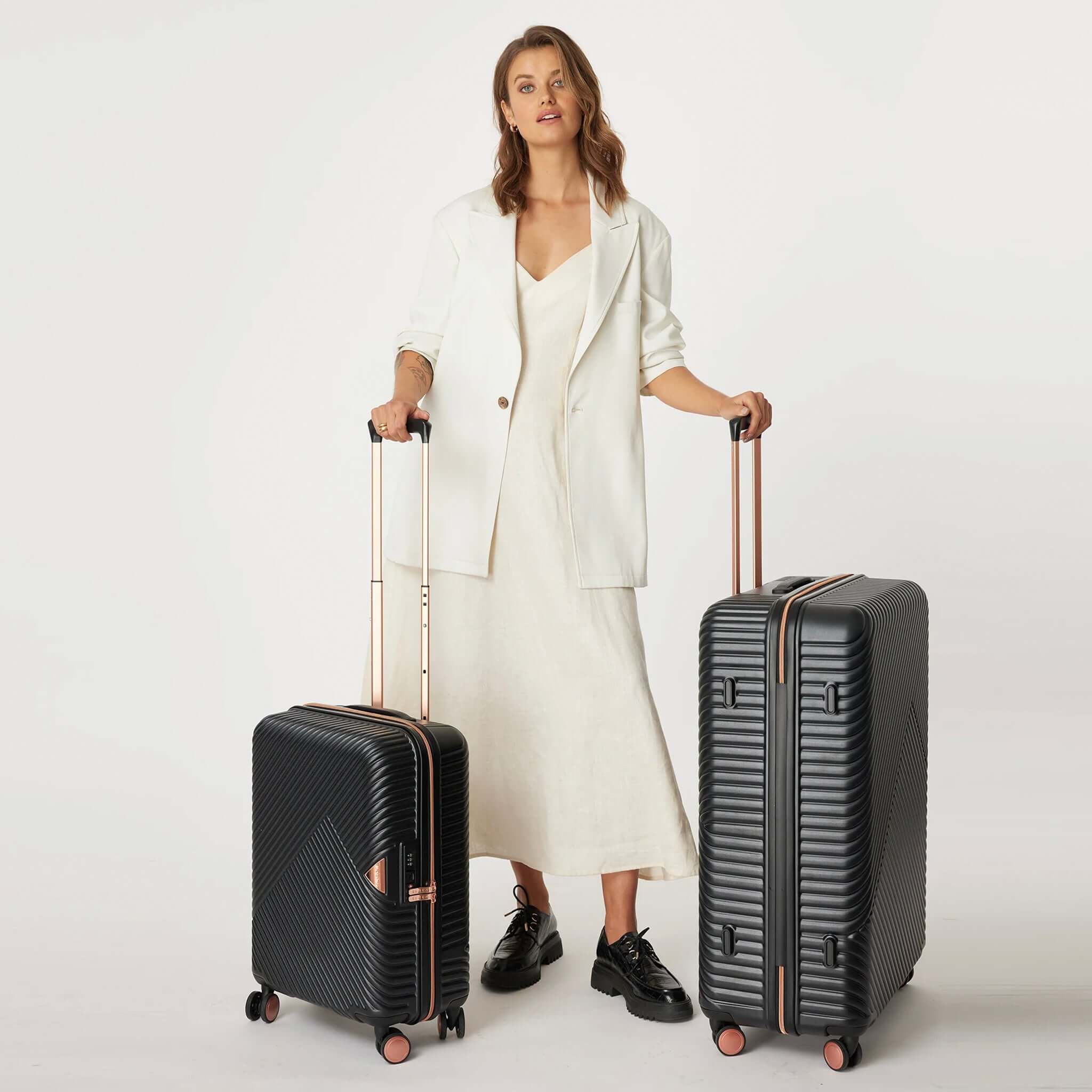 Woman with a set of two black moulded polycarbonate suitcases with metallic rose gold detailing, featuring a retractable handle and dual spinner wheels.