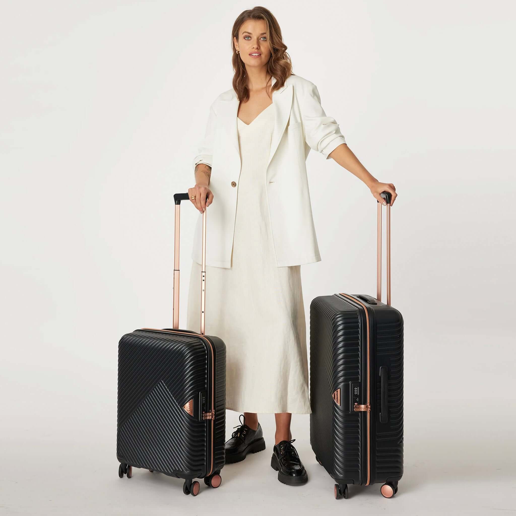 Woman holding on to a set of two black moulded polycarbonate suitcases with metallic rose gold detailing, featuring a retractable handle and dual spinner wheels.