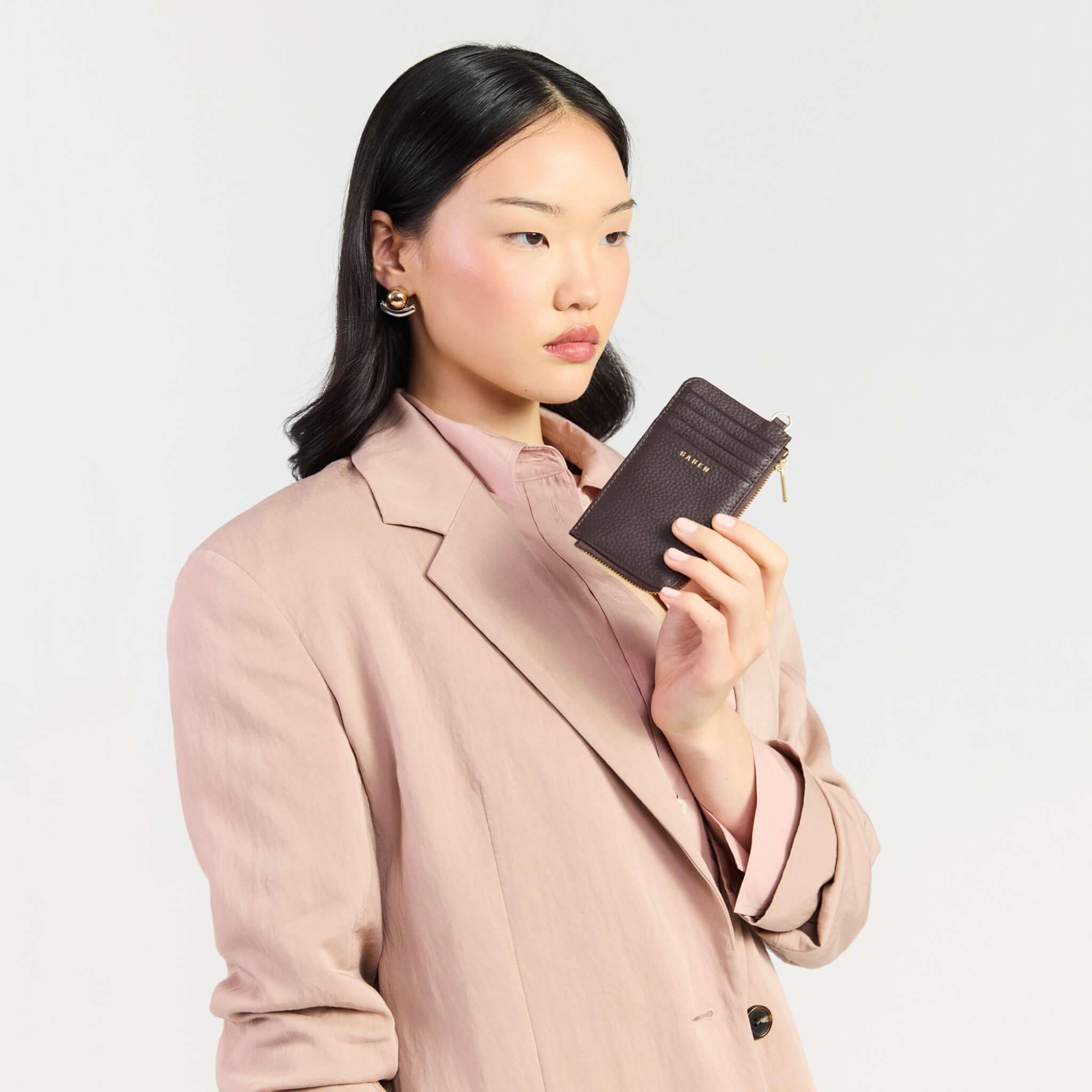 Saben Winona Card Holder - Cacao held by a model wearing a light pink blazer, showcasing its sleek design.