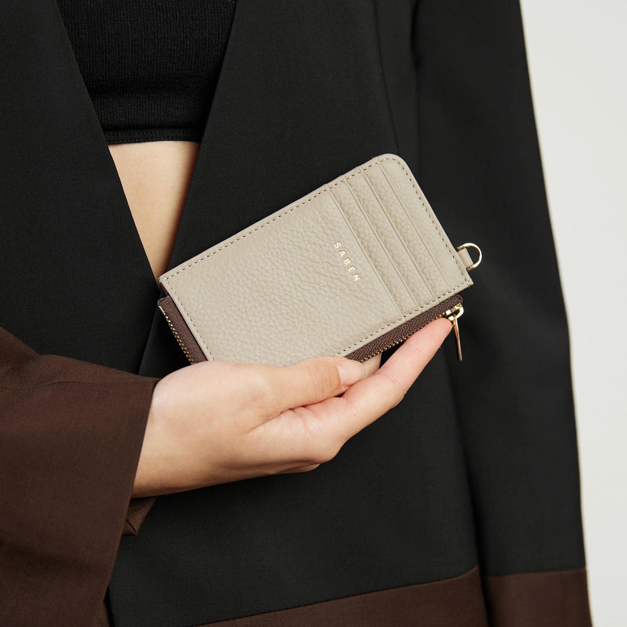 Hand holding a beige wallet with a dark coat in the background