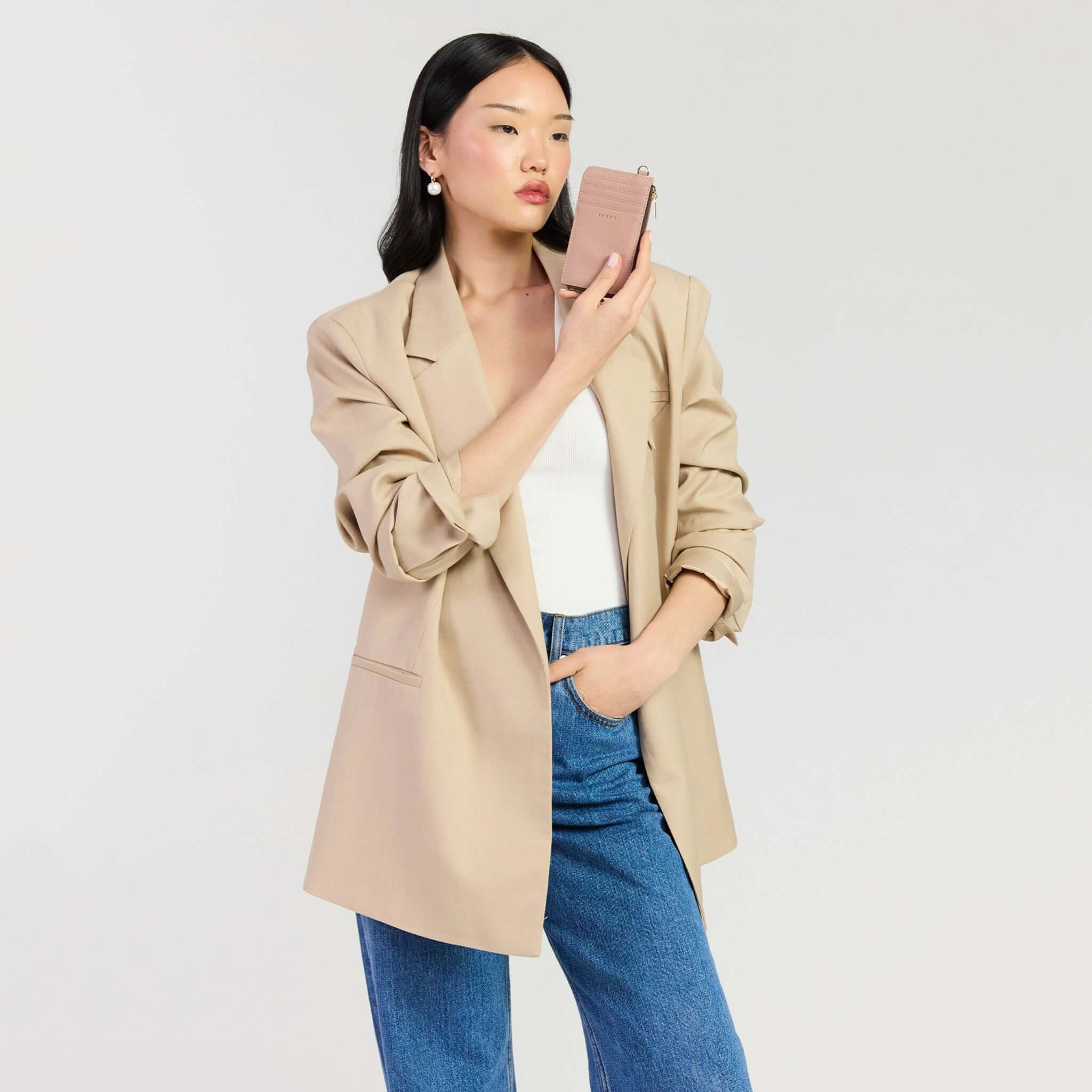 A woman in a beige blazer holding the Saben Winona Card Holder - Rosewater against a neutral background.