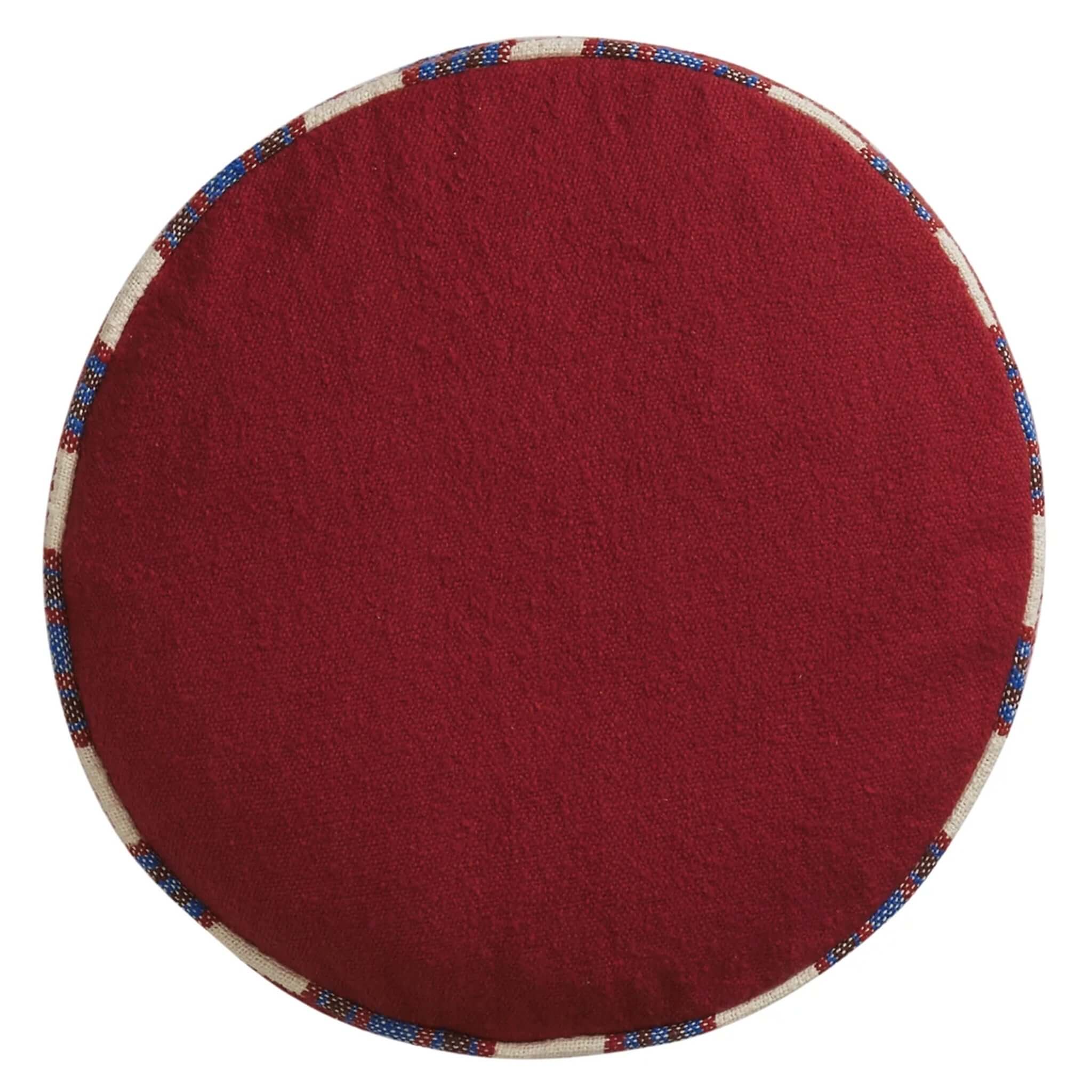 Round red cushion with a patterned border on a white background