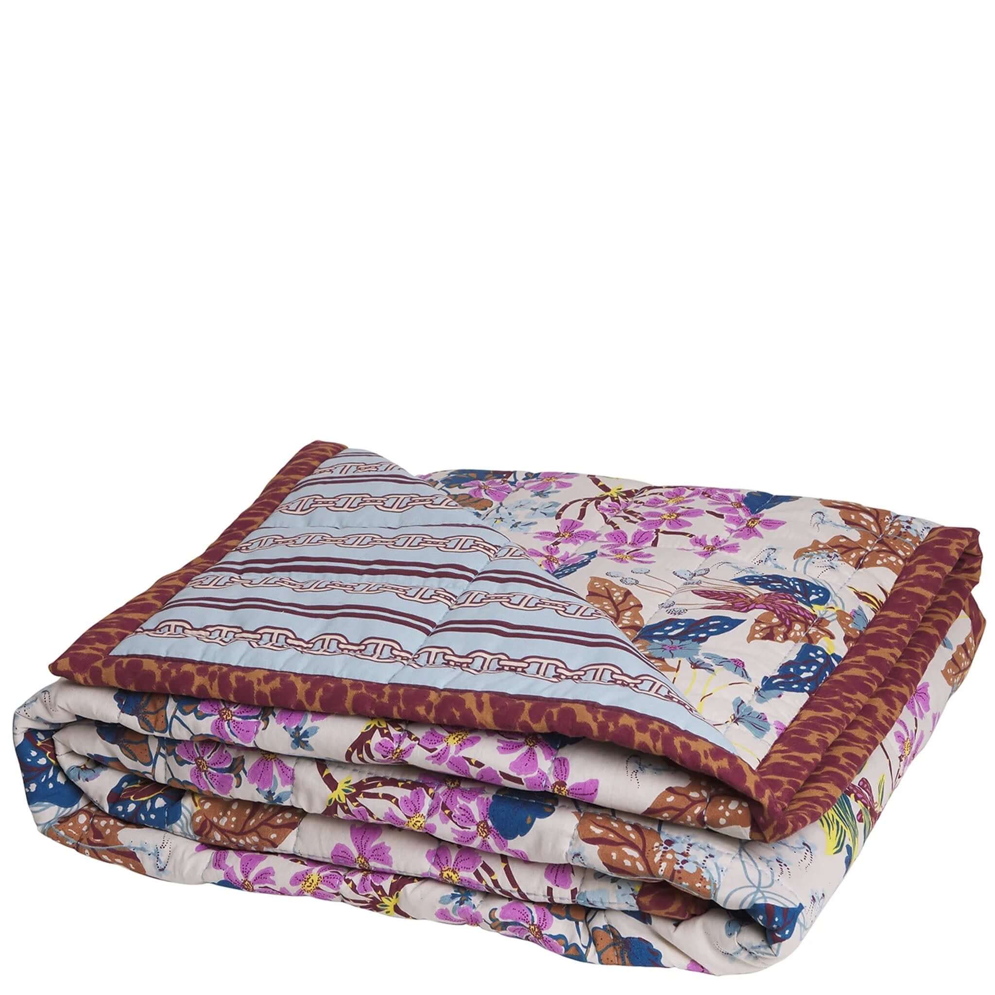 A folded multicolored floral blanket with a mix of animal patterns, featuring a combination of flowers and geometric shapes in a mix of beige, white, and dark colors.