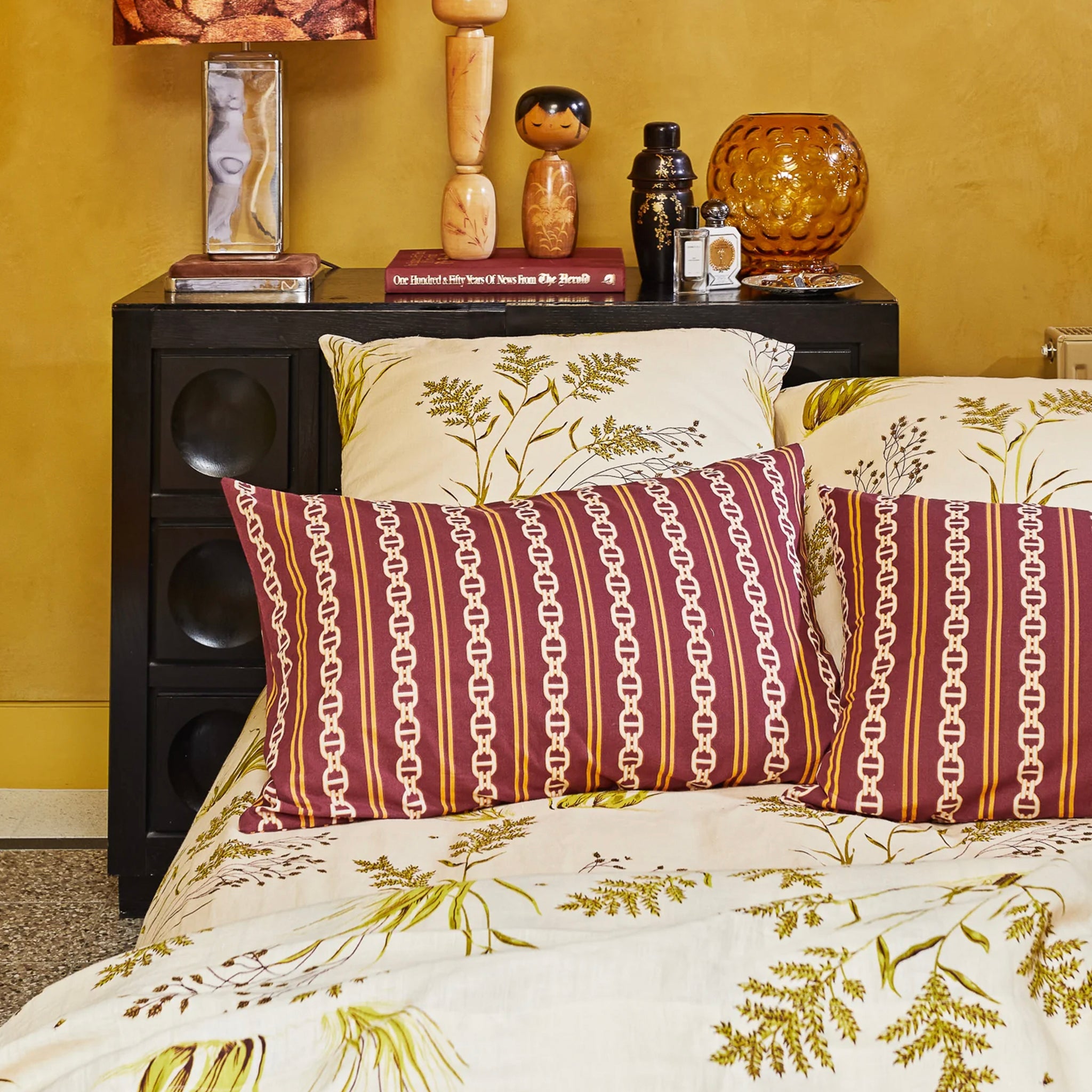 A mahogany-colored organic cotton pillowslip with a geometric pattern featuring a stripe and chain design on a bed.