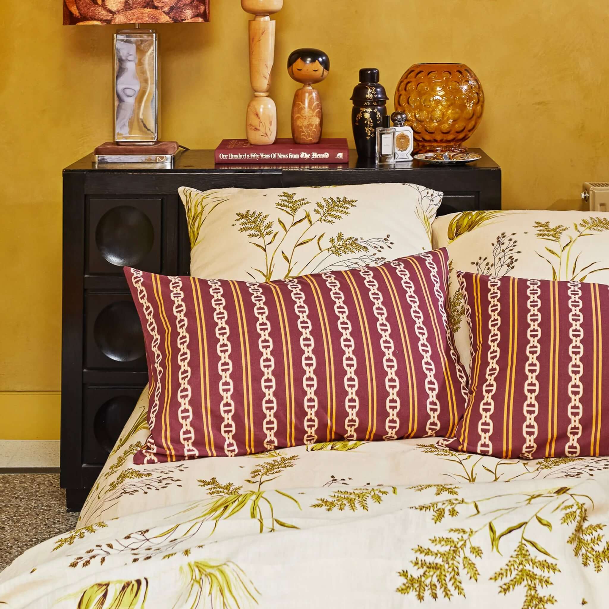 A mahogany-colored organic cotton pillowslip with a geometric pattern featuring a stripe and chain design on a bed.