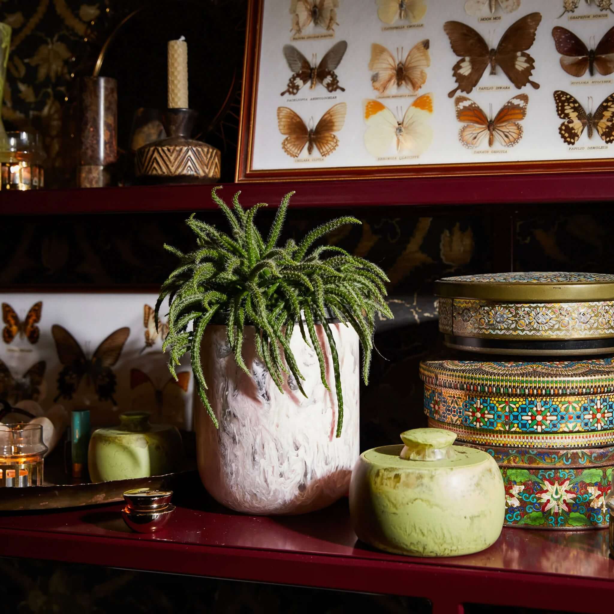 A hand-poured pink resin vase with a mid-century inspired design on a shelf.
