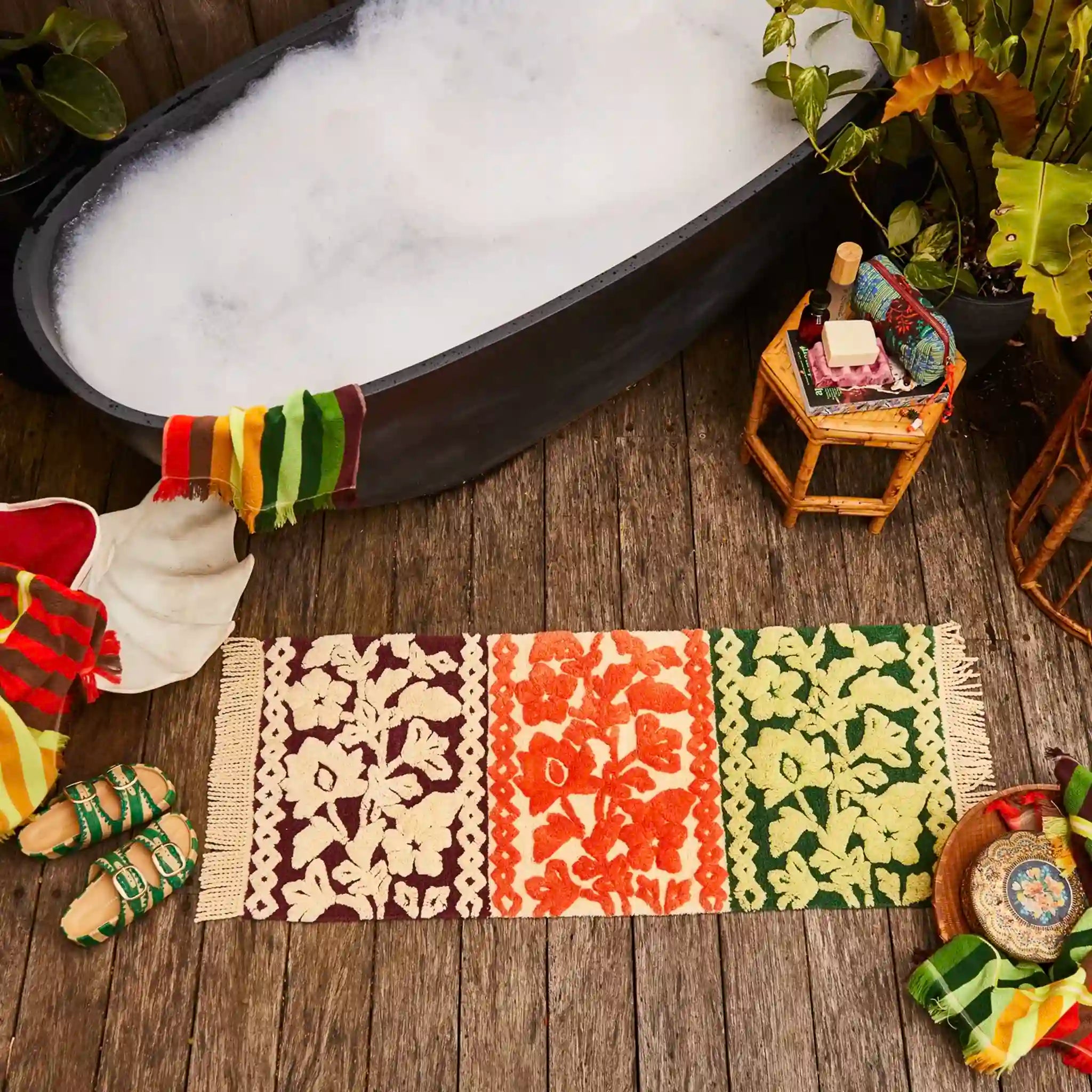 Decorative bath mat with floral patterns on a wooden floor next to a bathtub filled with bubbles.