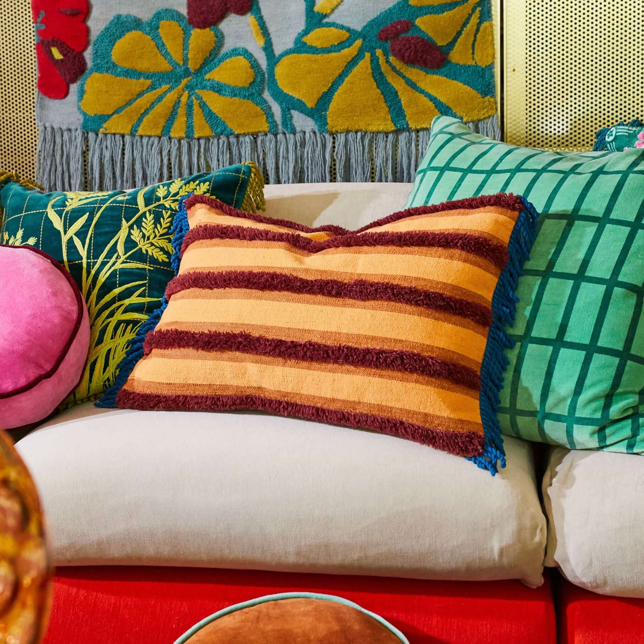 A rectangular cushion with a striped pattern in beige, brown, and blue colors, featuring hand-tufted detailing and fringe edges.