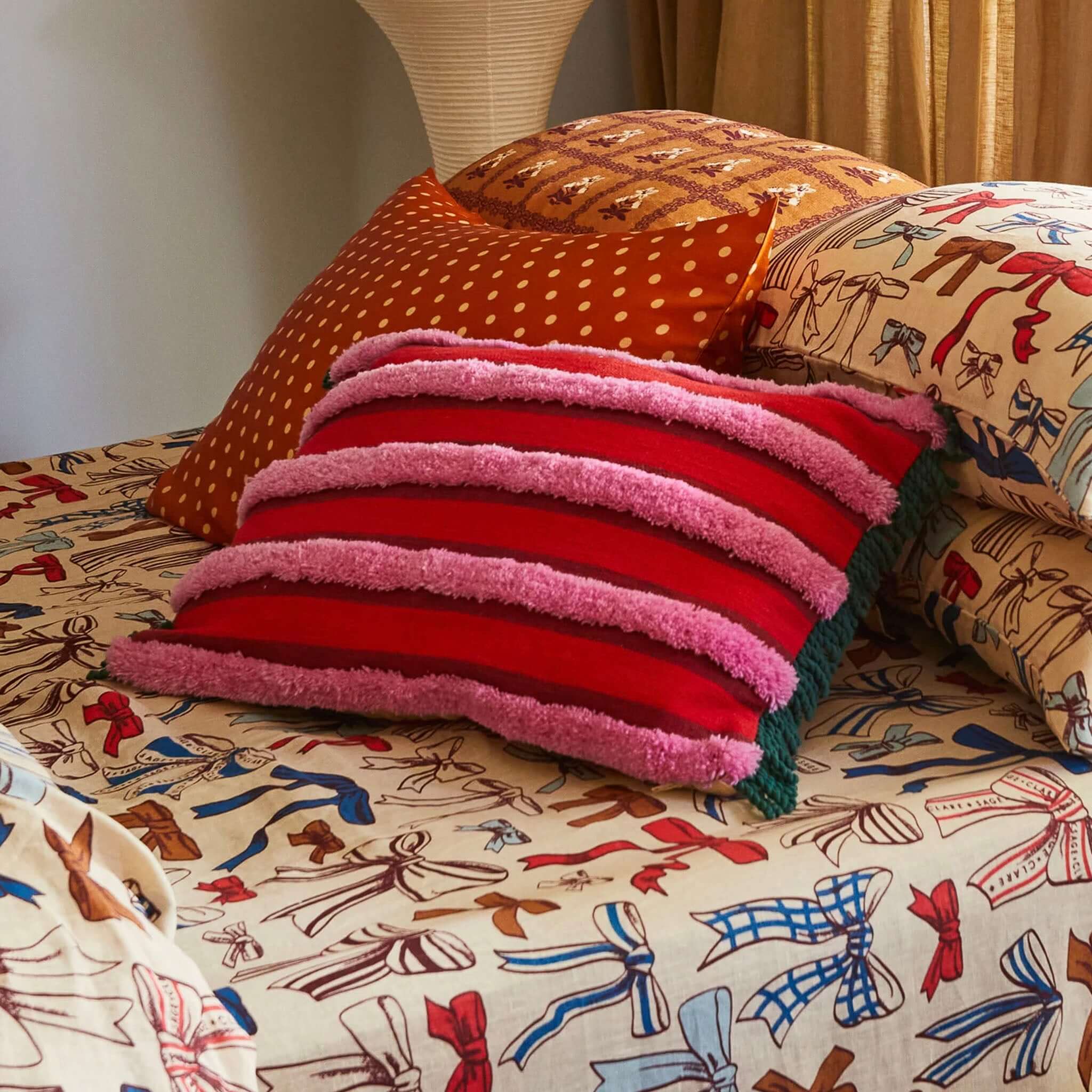 A rectangular tufted cushion with red and pink stripes and green fringe edges.