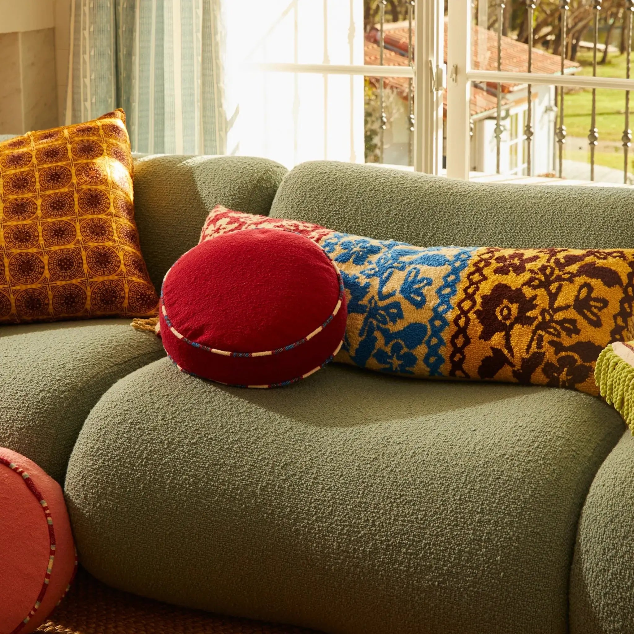 Green sofa with colorful cushions in a bright room with large windows.
