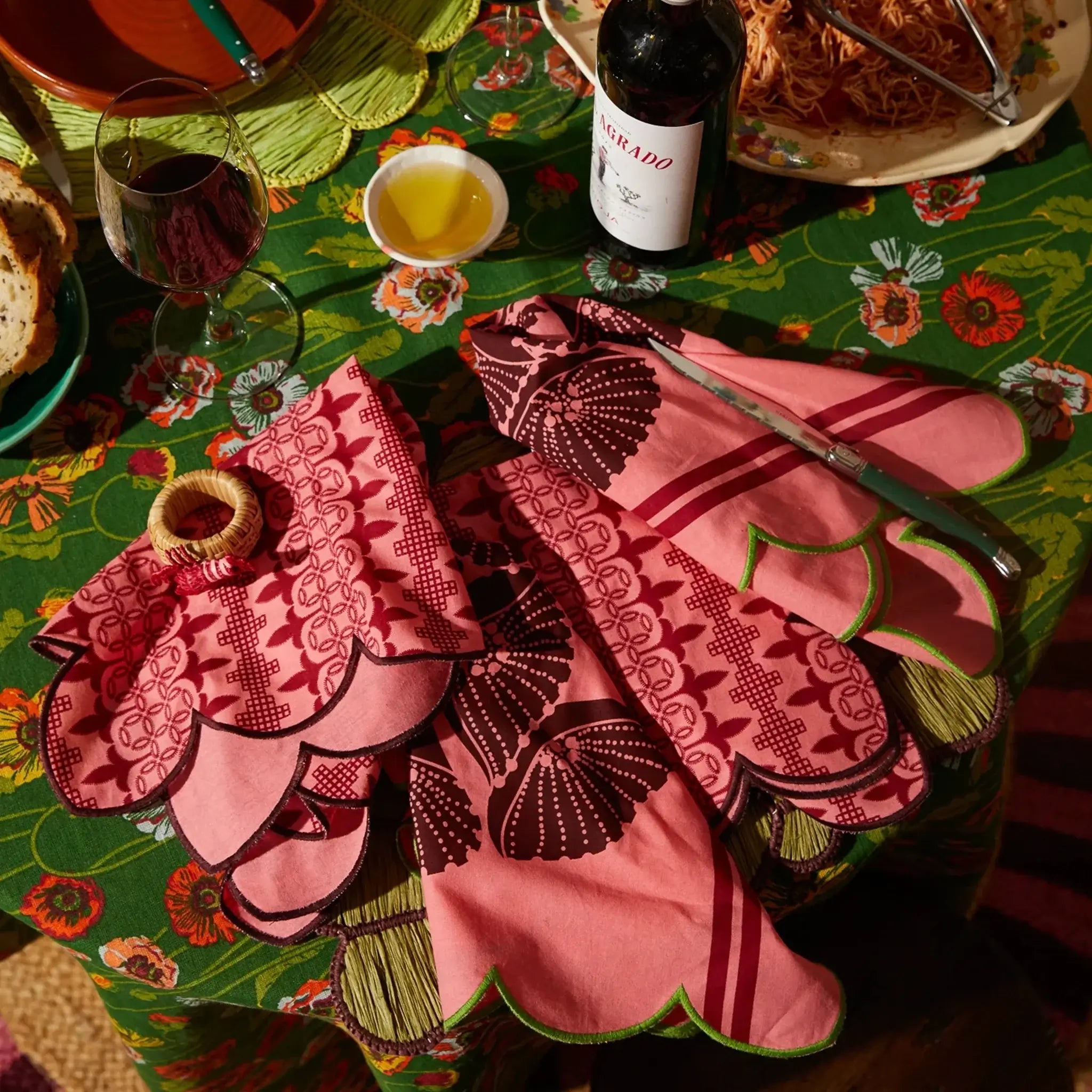 Decorative pink and black embroidered tablecloth on a colorful table with wine glasses and food.