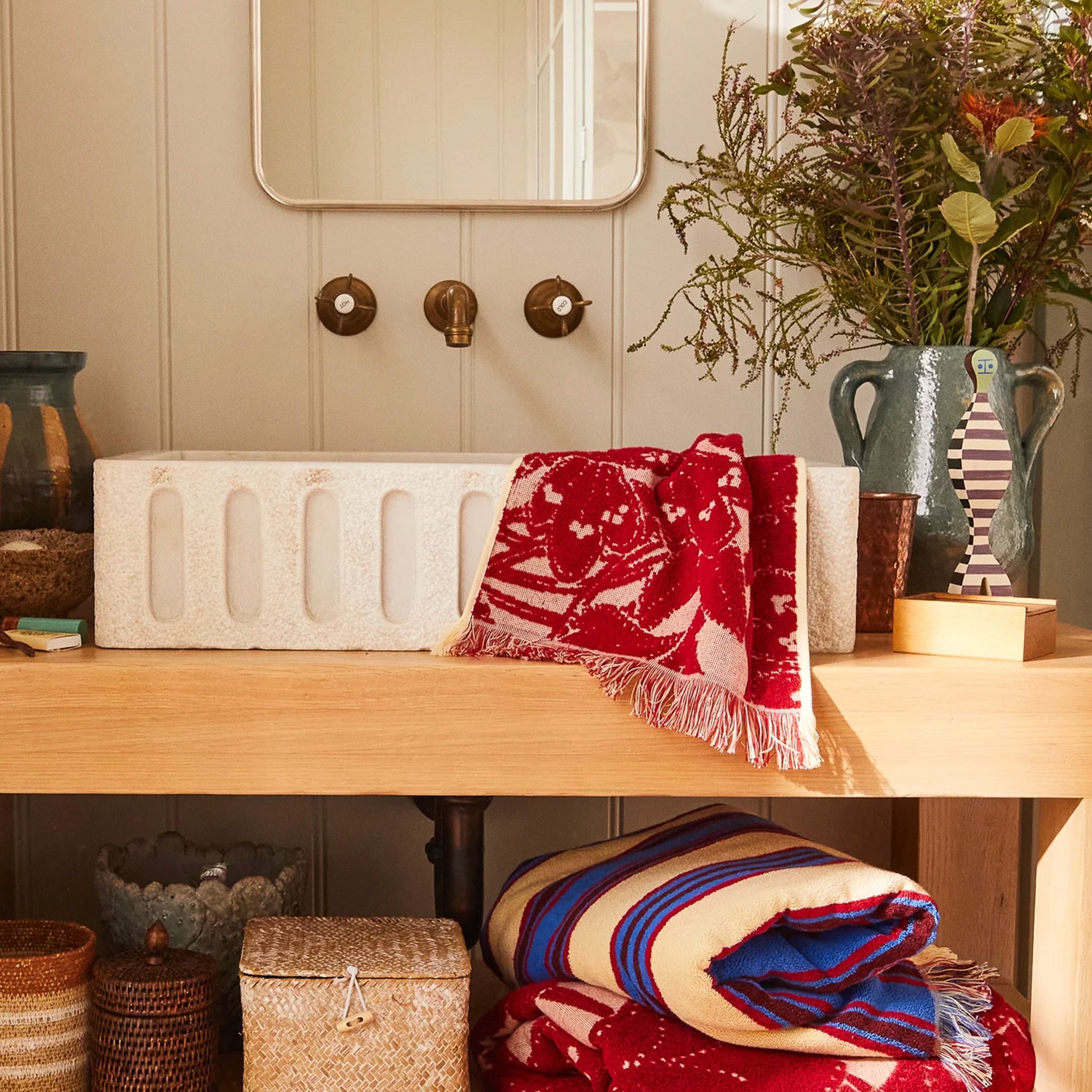 Decorative scene with a red patterned blanket on a wooden surface, surrounded by vases and plants.