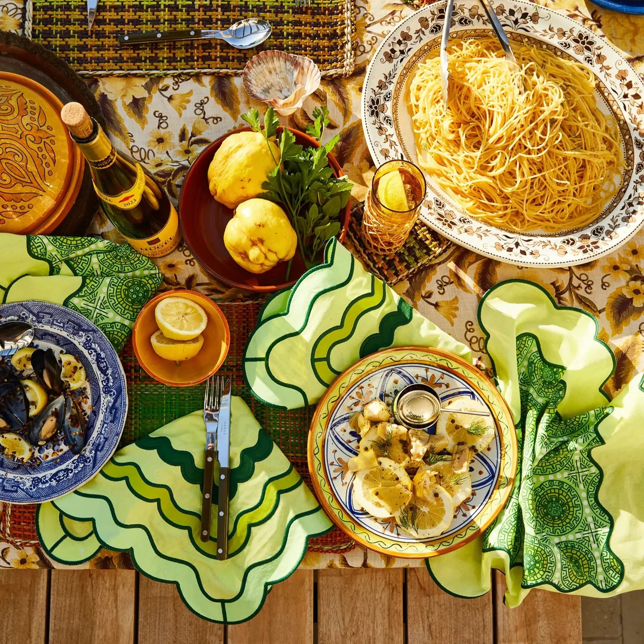 Dining table set with Italian-themed plates, pasta, and lemons on a wooden surface.