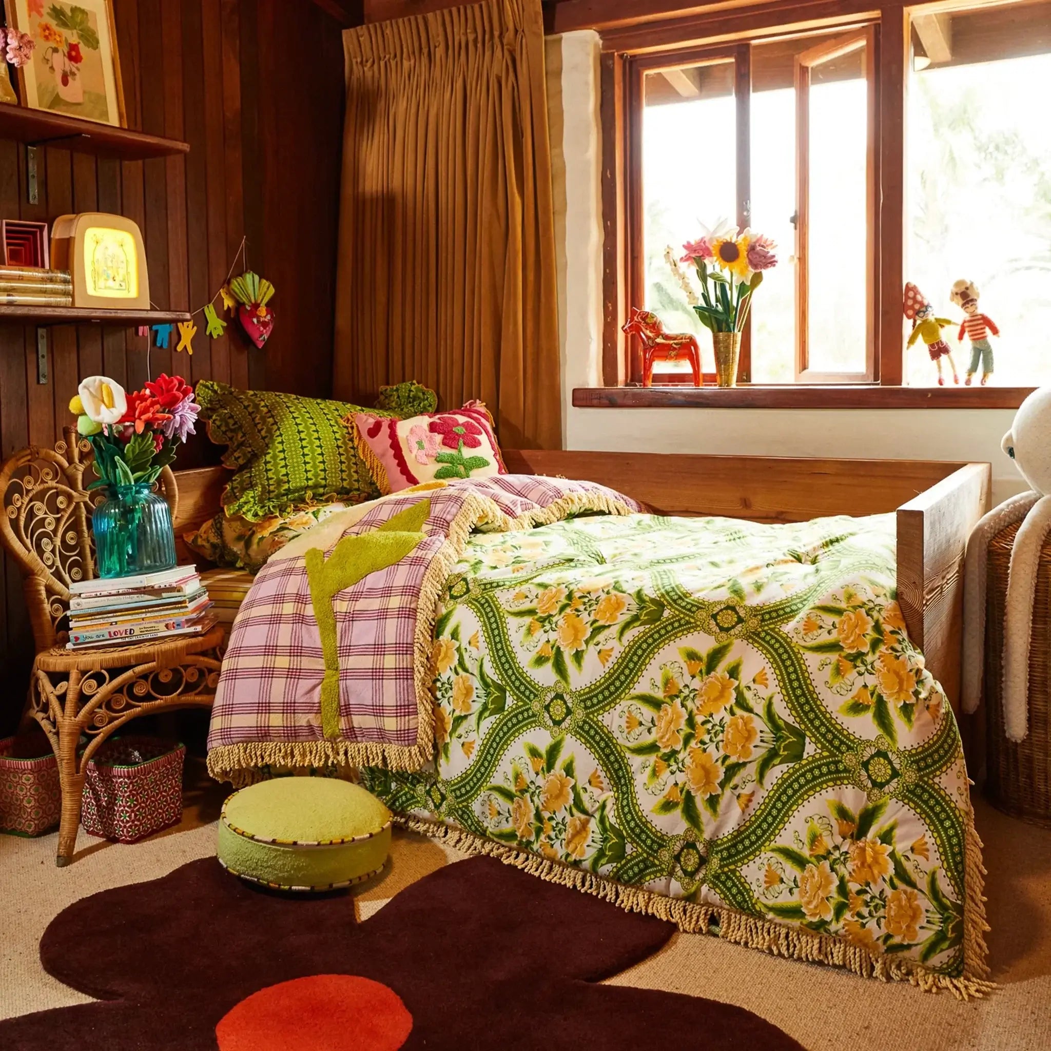 Cozy bedroom with floral bedding, colorful pillows, and a window with sunlight streaming in.