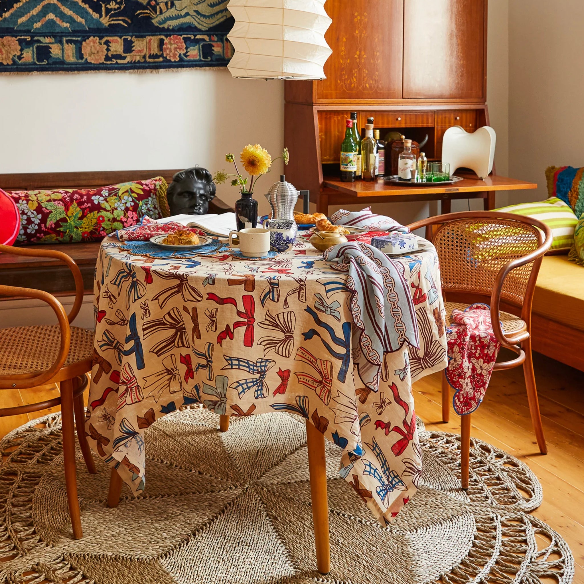A linen tablecloth with a pattern of colorful bows in red, blue, and brown colors on a beige background on a table.