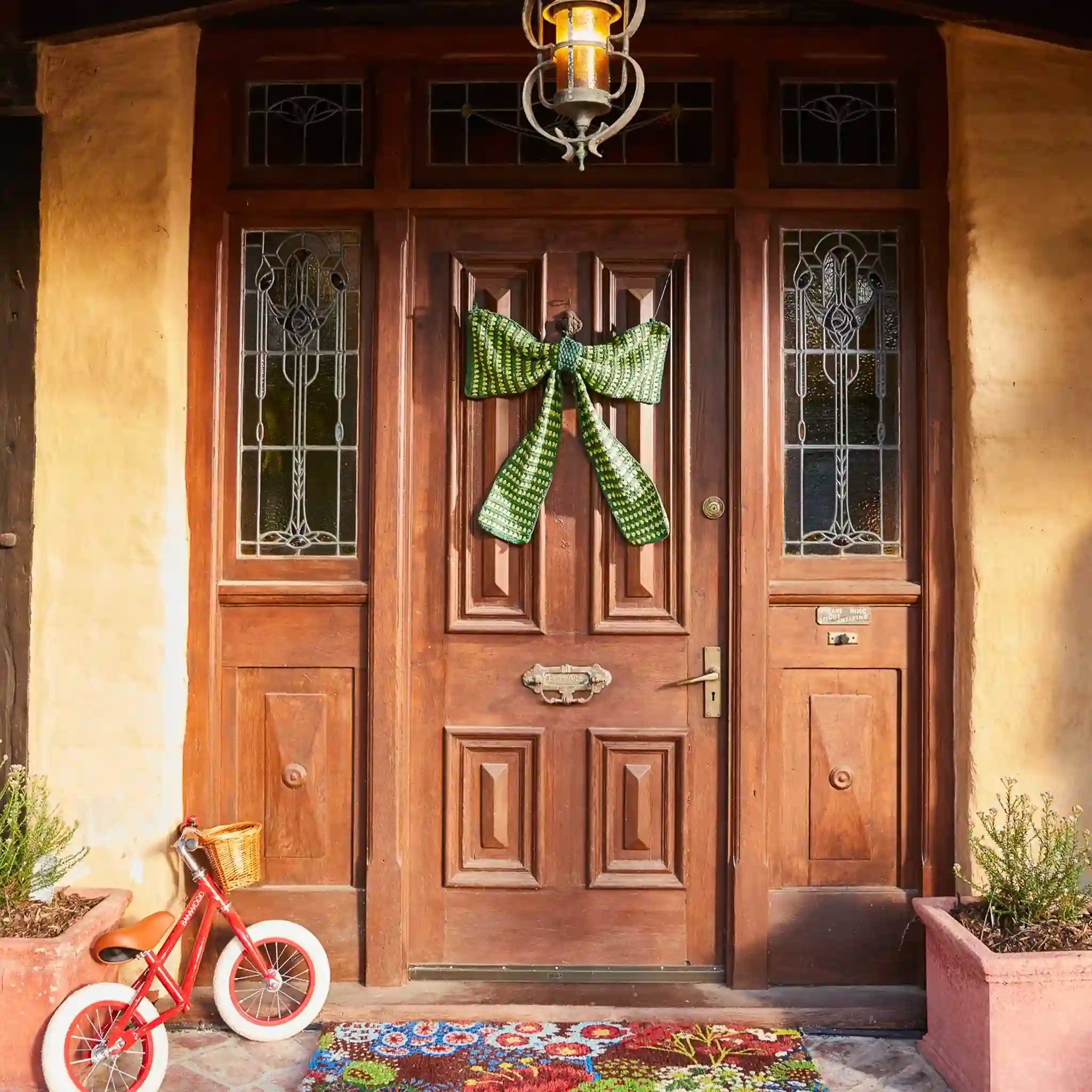 Wooden front door with decorative green bow, red bicycle, and colorful rug.