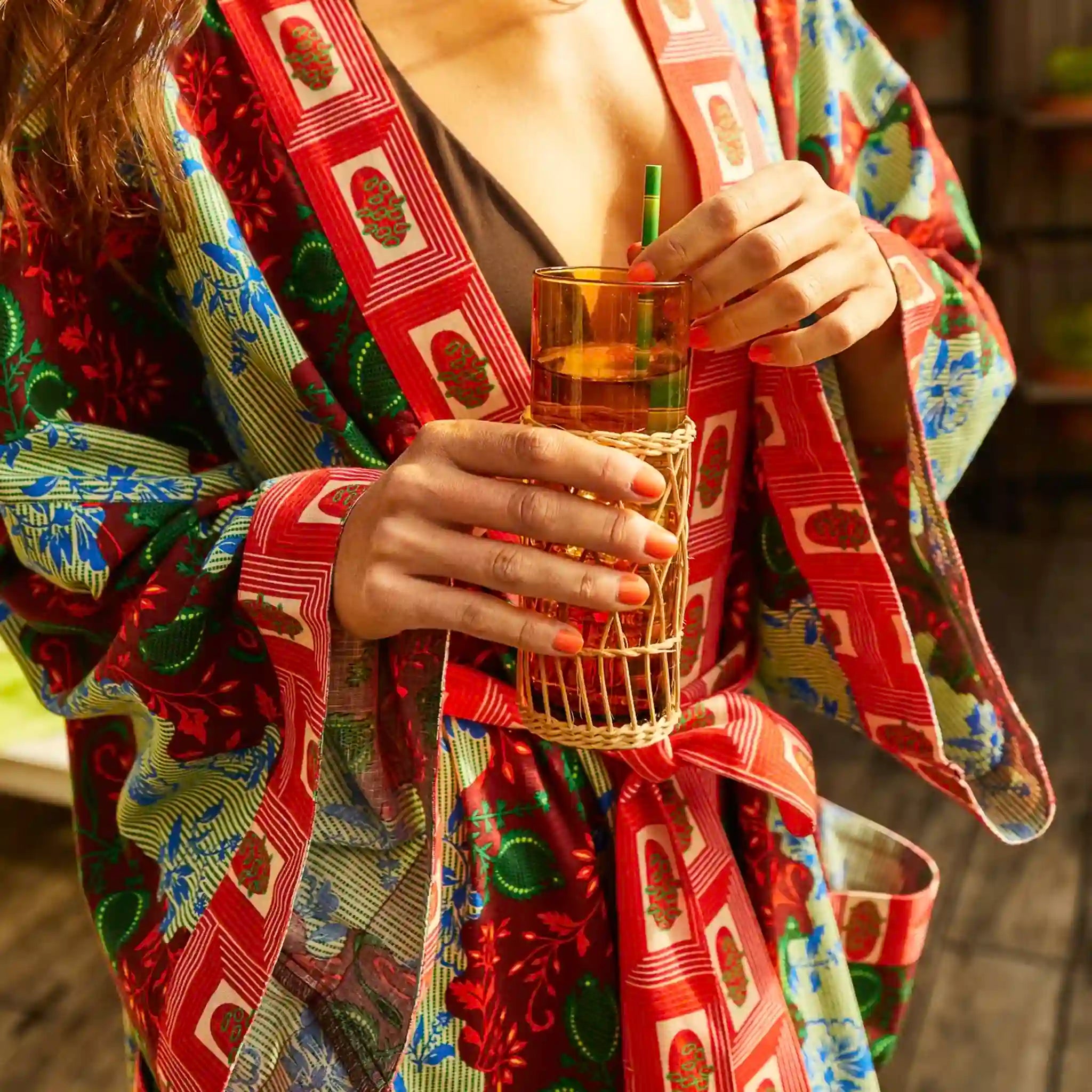Person wearing a colorful kimono holding a woven glass with a straw.