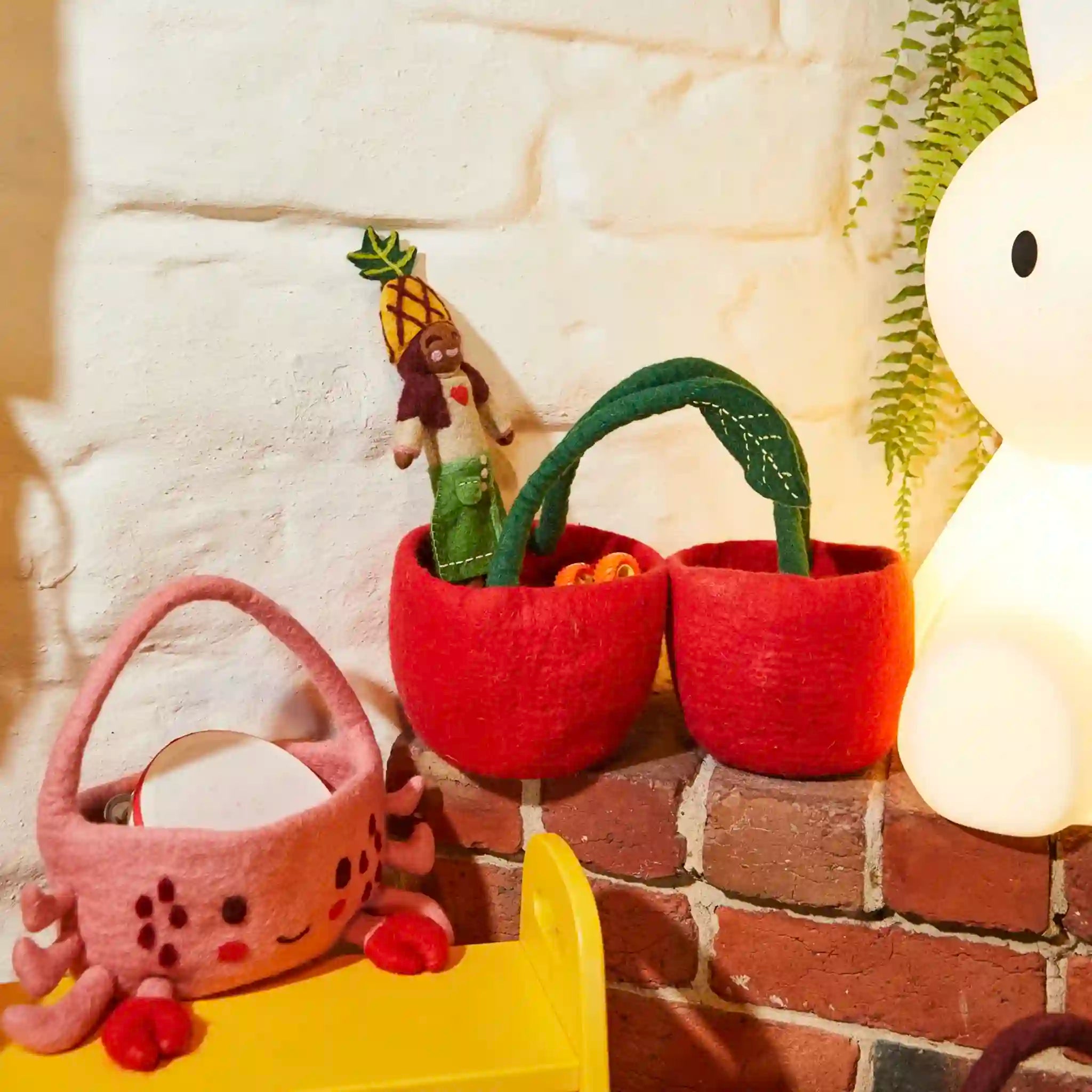 Plush toys resembling plants and a basket against a brick wall.