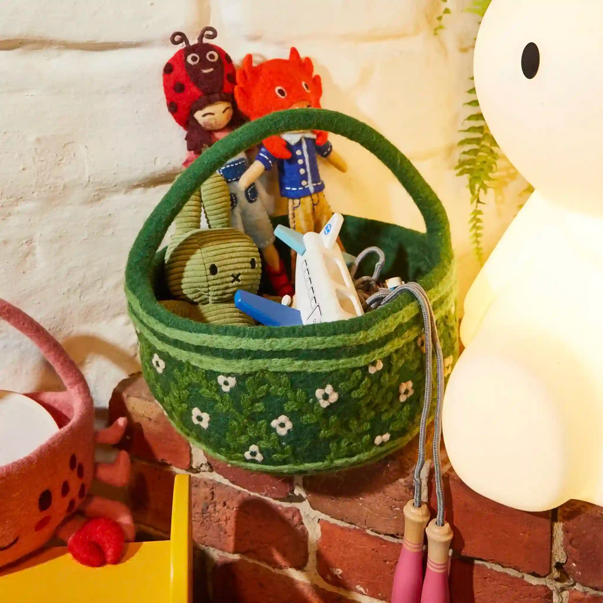 Green felt basket with small toys and items on a textured surface