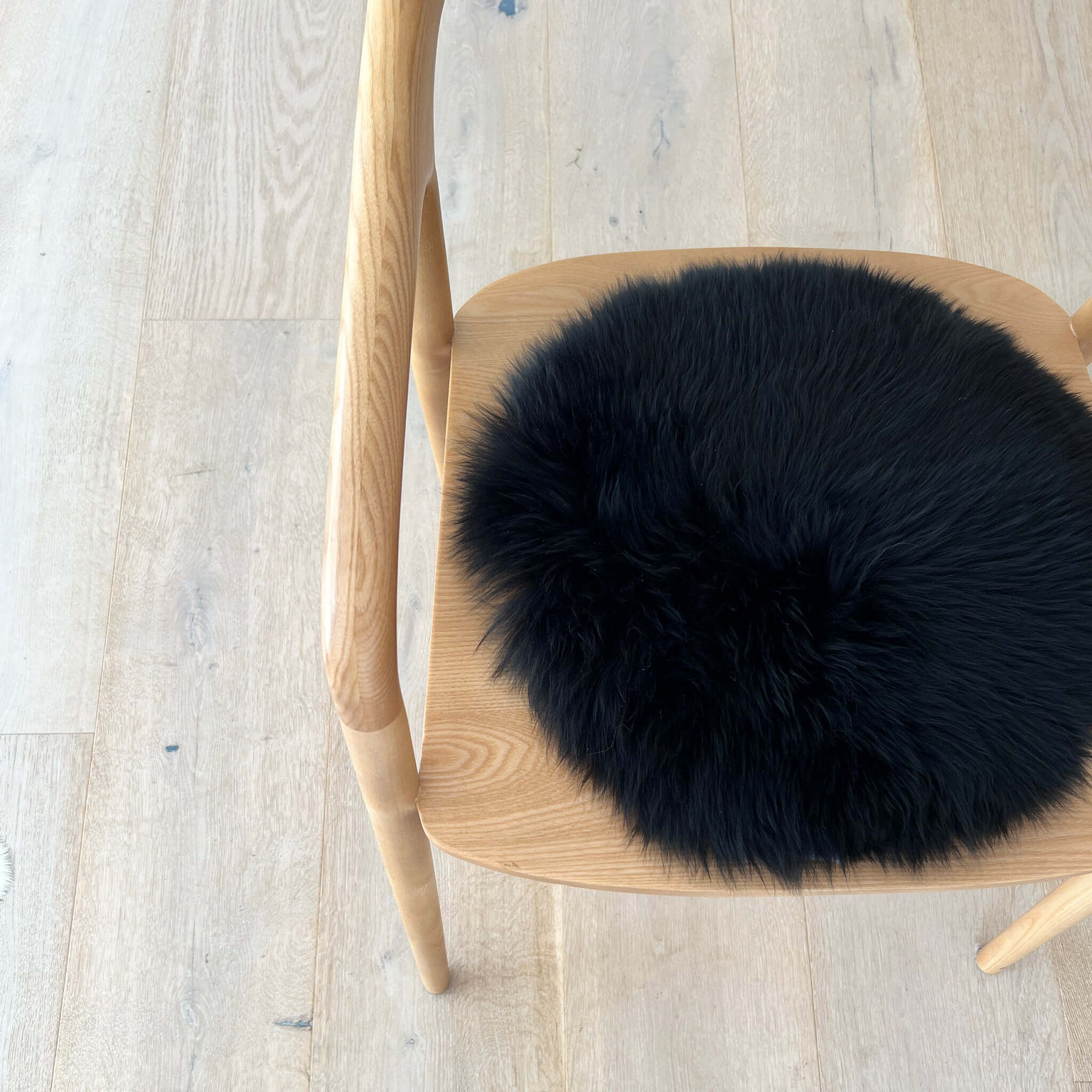Alt Tag: Long Wool Sheepskin Circle Chair Pad - Black on wooden chair, round black long wool sheepskin seat pad